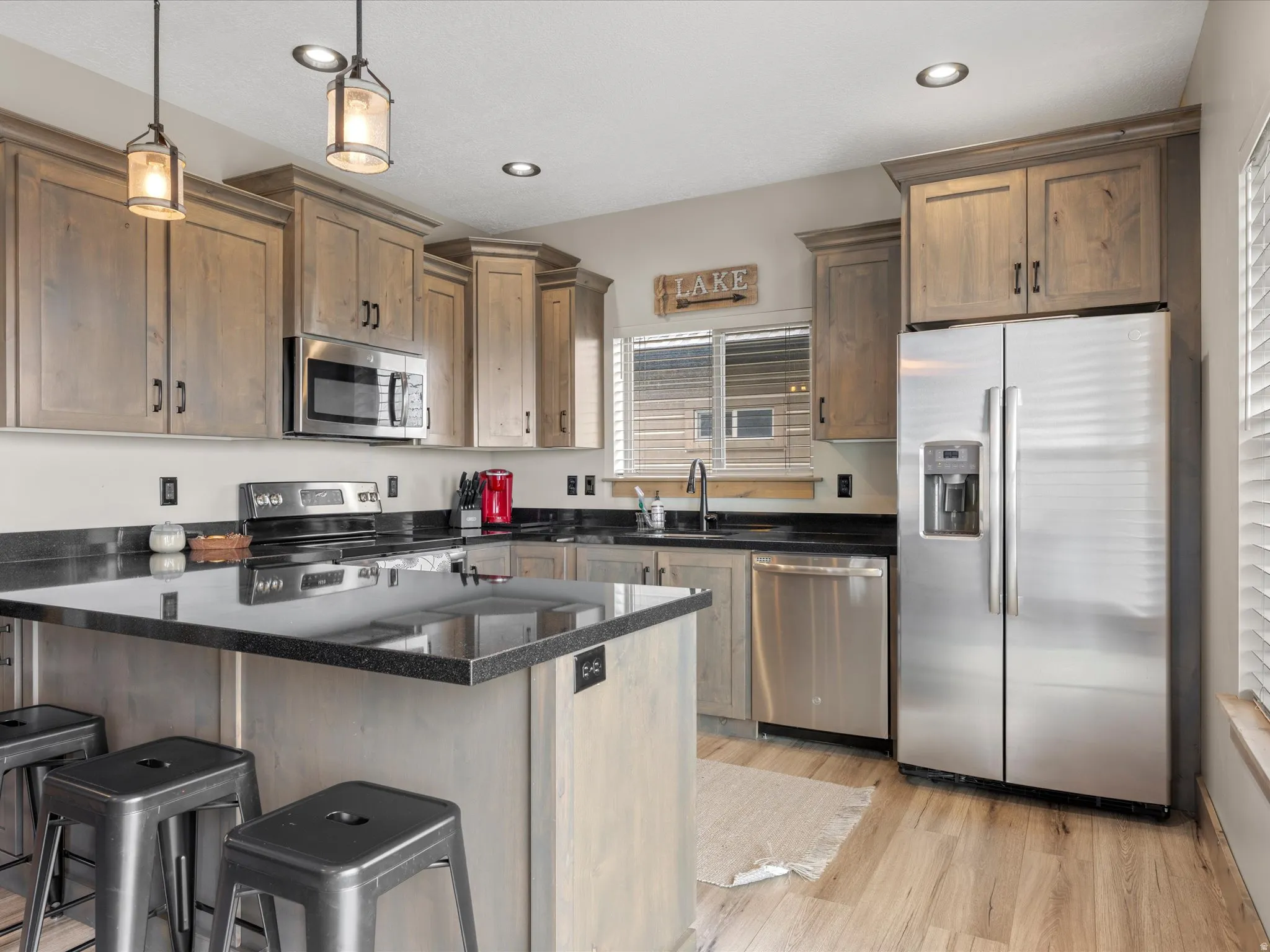 Kitchen featuring stainless steel appliances, a breakfast bar, dark stone counters, light wood-style flooring, and decorative light fixtures