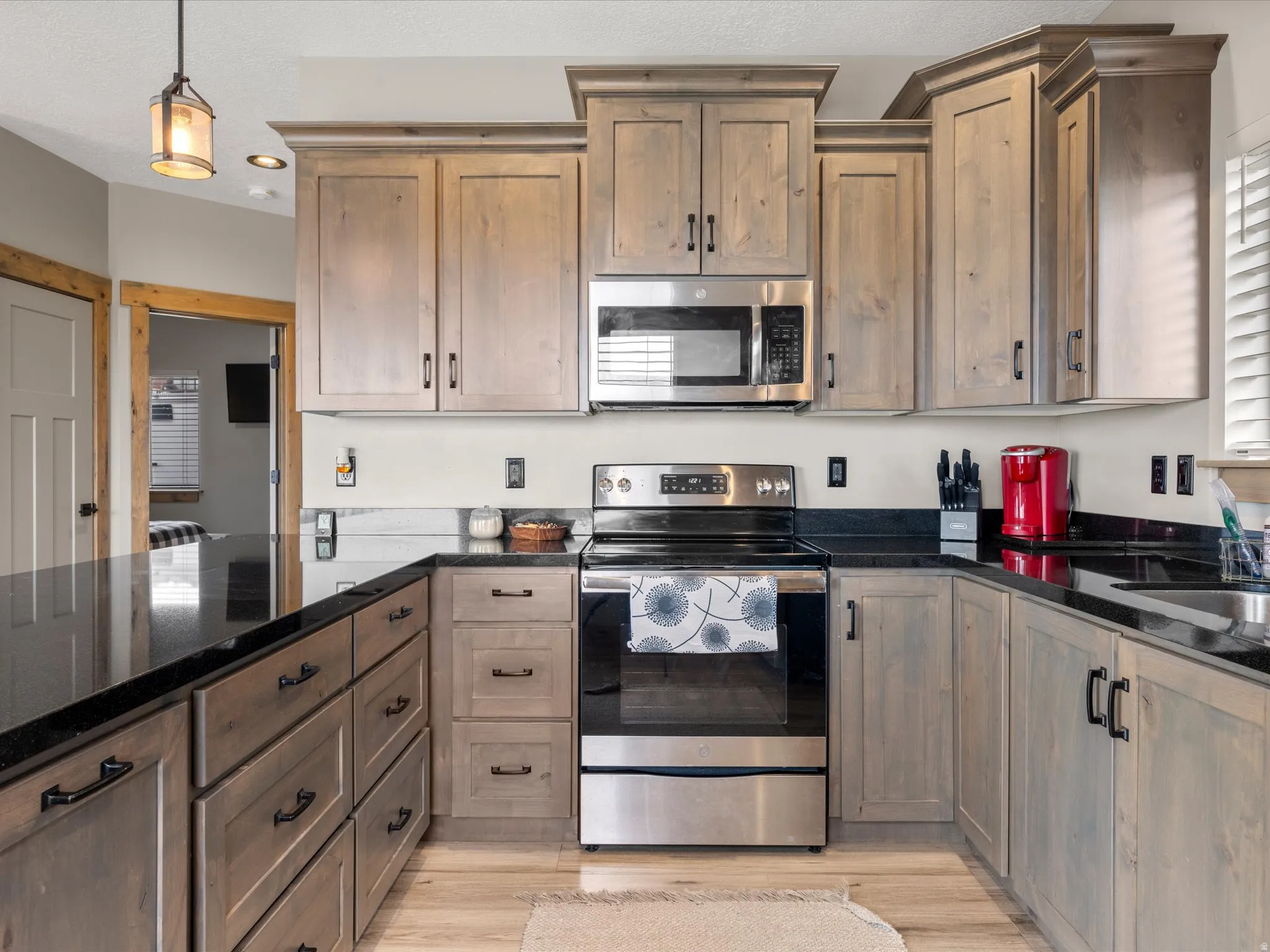 Kitchen with stainless steel appliances, dark stone counters, pendant lighting, and light wood-style floors