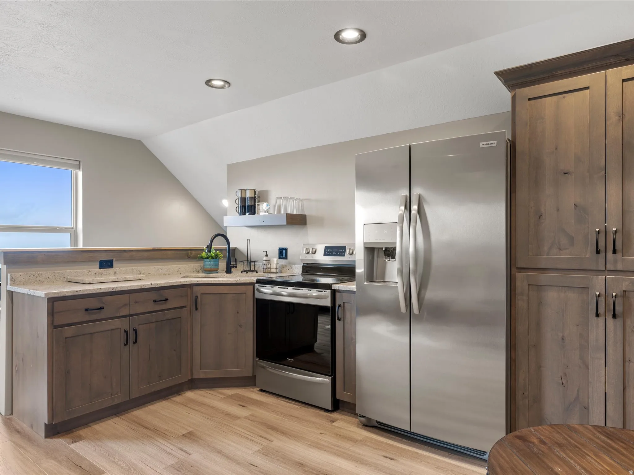Kitchen featuring stainless steel appliances, a peninsula, light wood-type flooring, dark wood finish cabinets, and light stone countertops