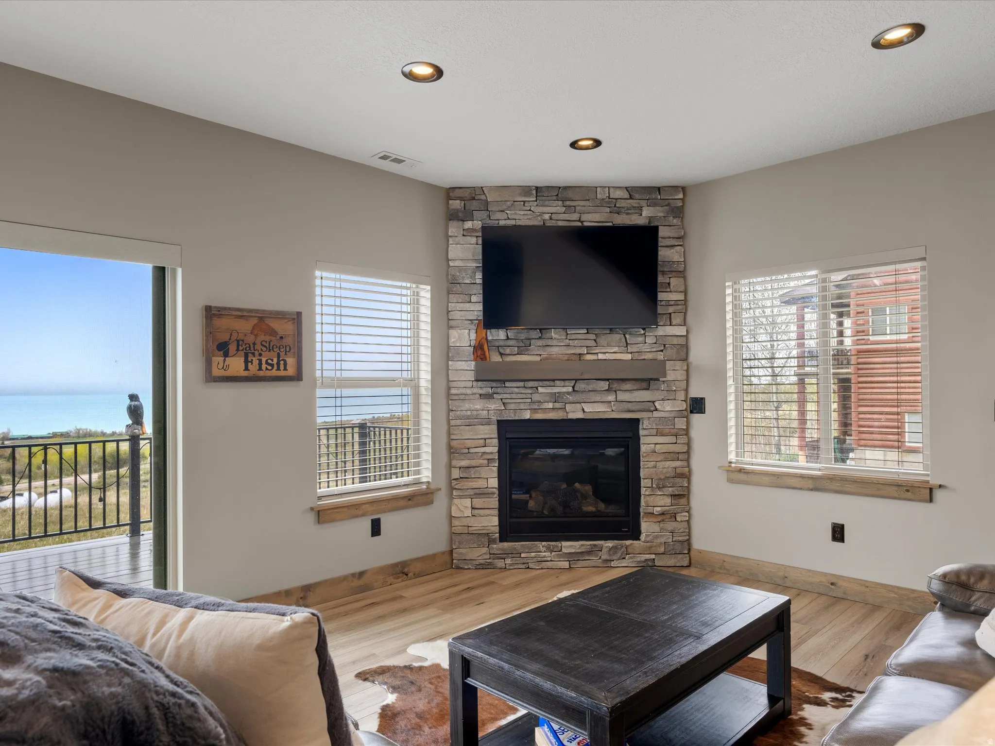 Living area with wood finished floors, a stone fireplace, and recessed lighting