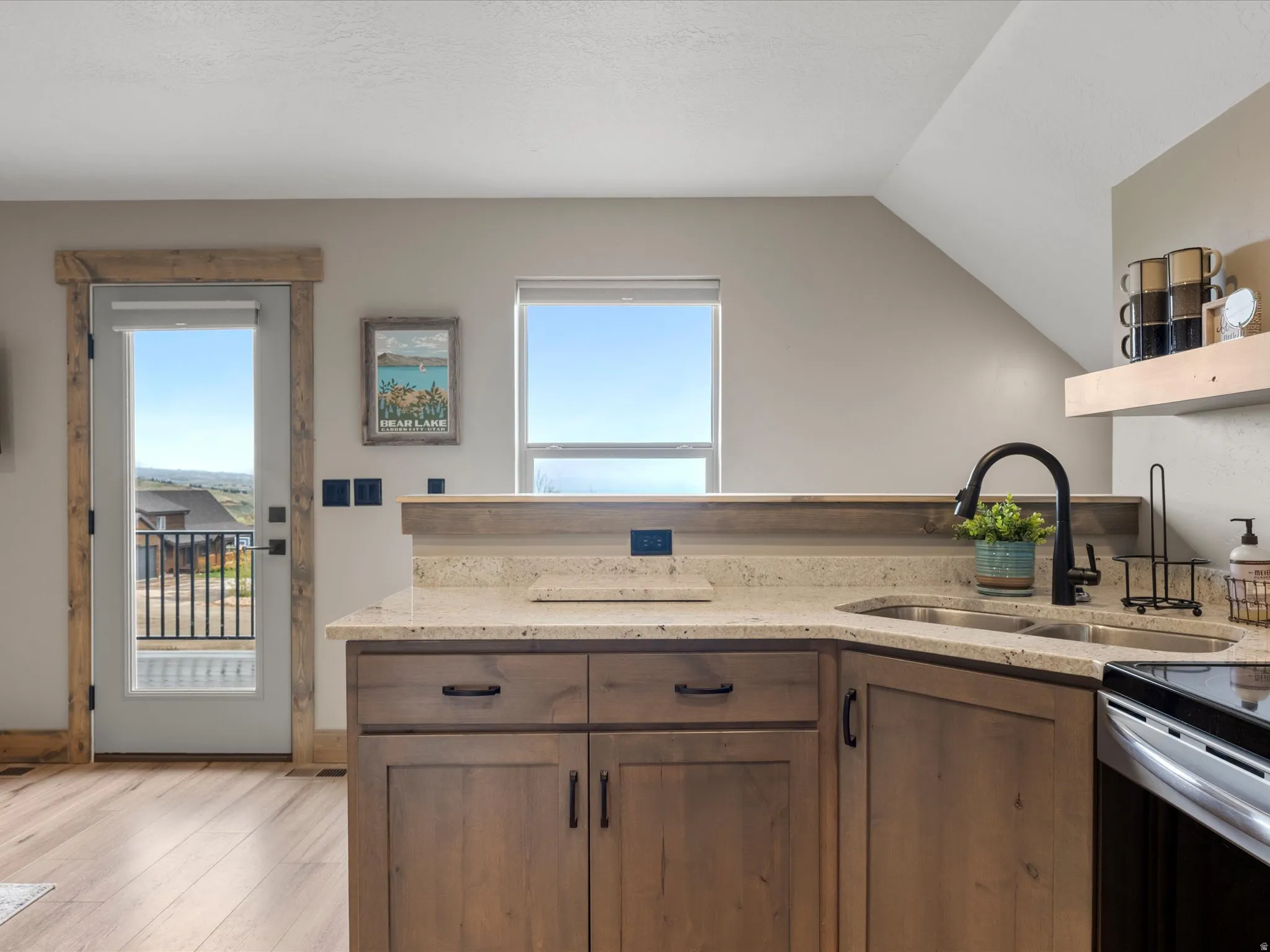 Kitchen featuring light stone countertops, healthy amount of natural light, light wood finished floors, and lofted ceiling