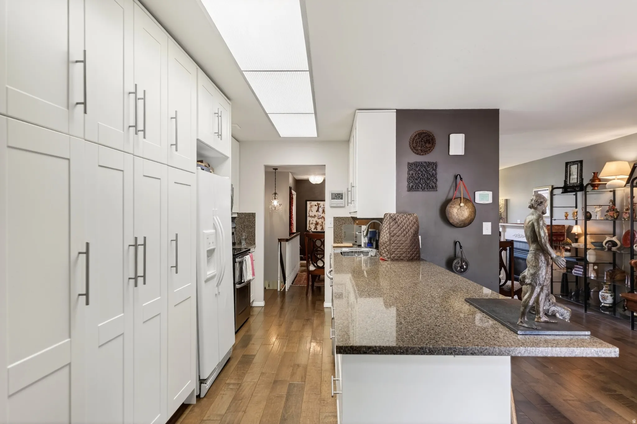 Kitchen with dark stone counters, dark wood-style floors, white cabinetry, a peninsula, and white refrigerator with ice dispenser