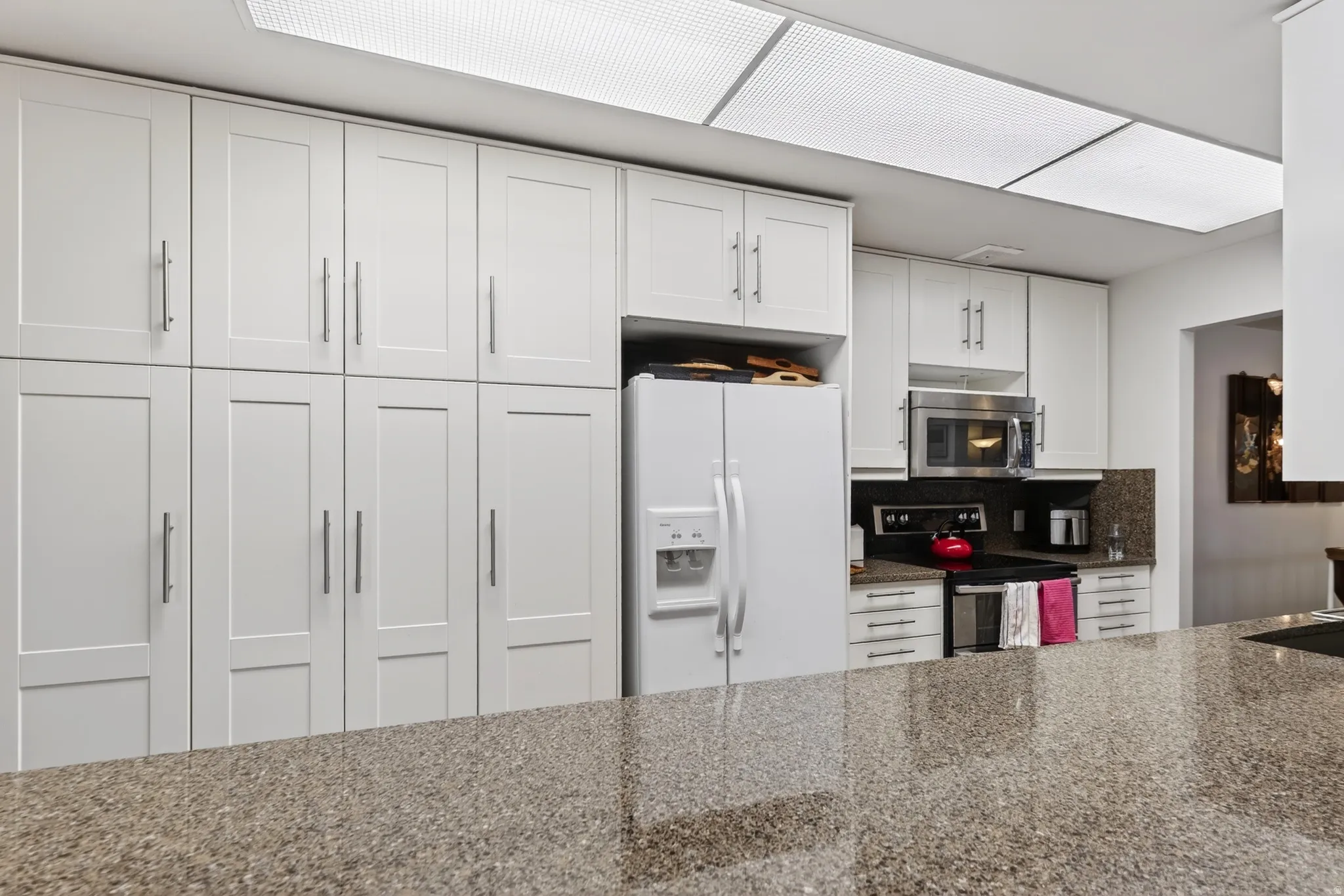 Kitchen with stainless steel appliances, white cabinetry, dark stone countertops, and decorative backsplash