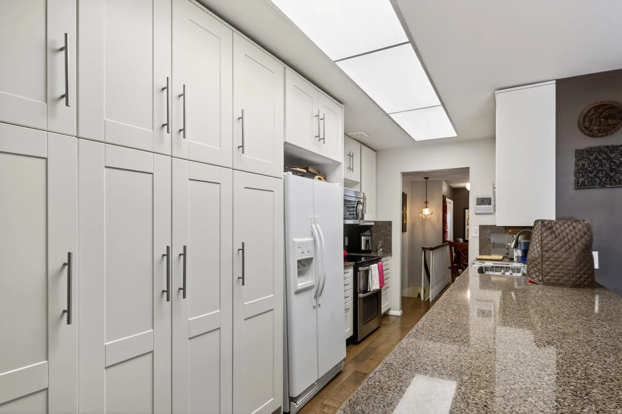 Kitchen featuring stainless steel appliances, white cabinets, and light stone countertops