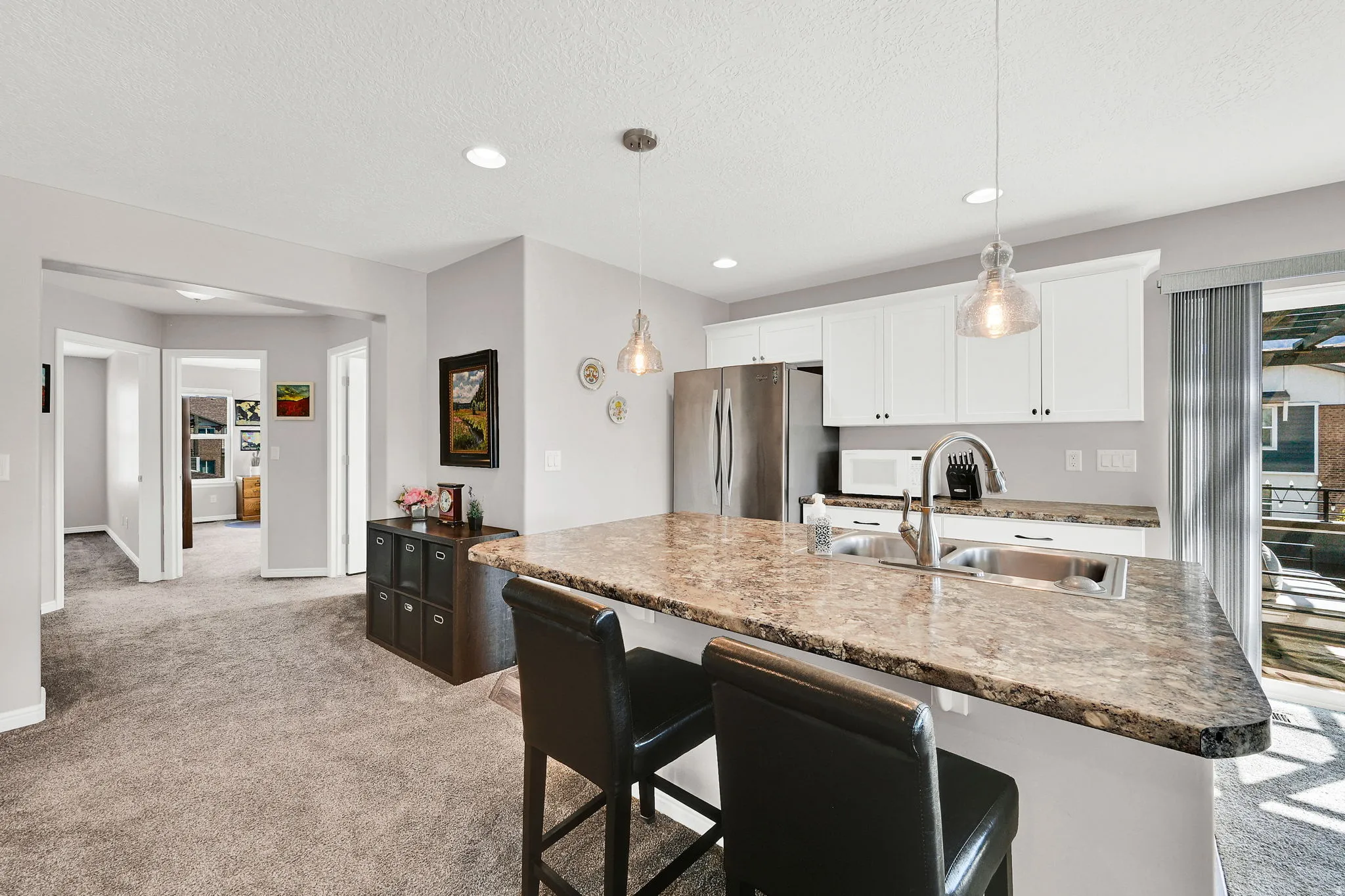 Kitchen area with a breakfast bar area, freestanding refrigerator, light carpet, white cabinets, and decorative light fixtures