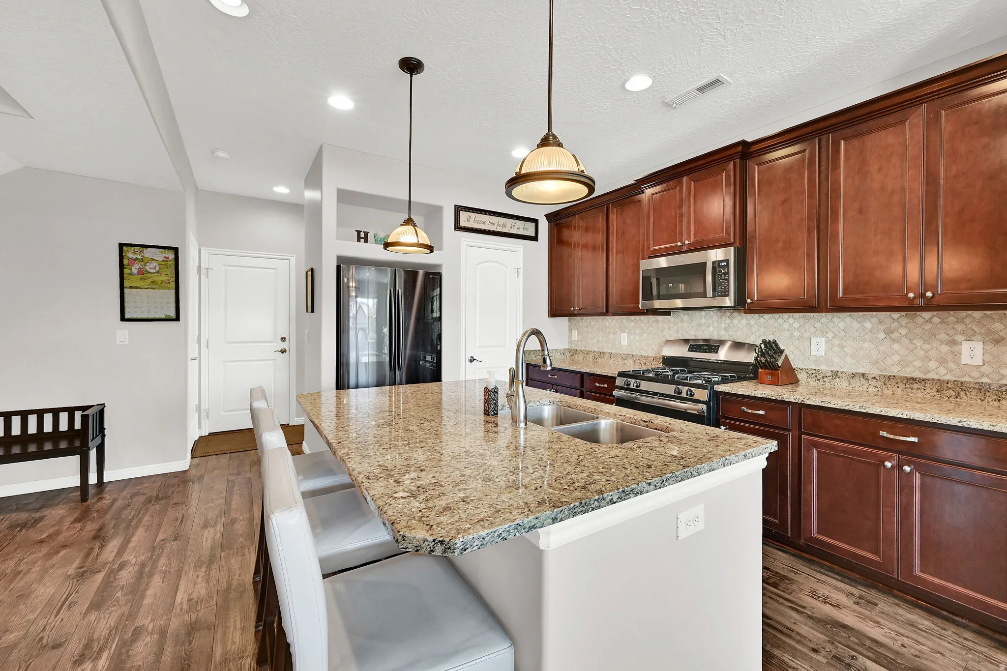 Kitchen featuring stainless steel appliances, light stone countertops, dark wood-type flooring, and a center island with sink