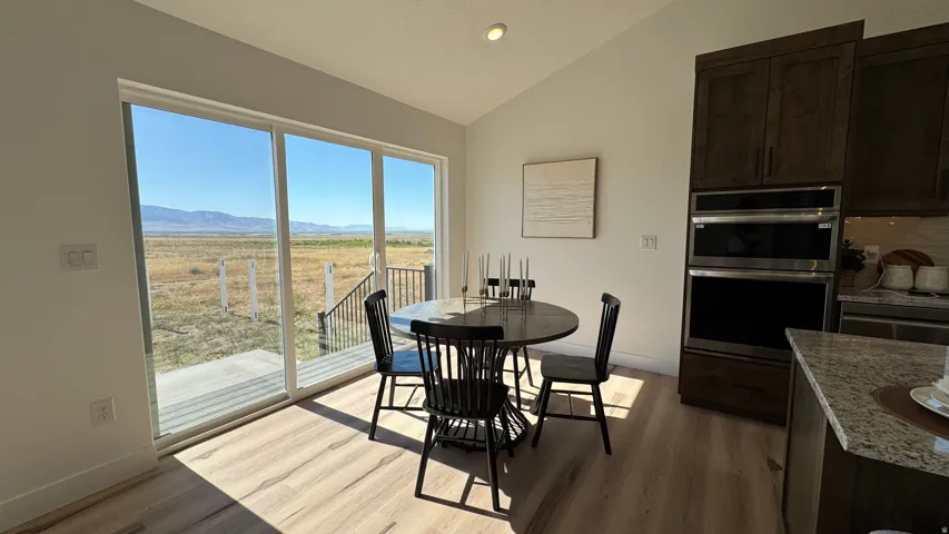 Spacious dining area featuring a sliding glass door, a large outdoor patio, wood-finish flooring, a built-in double oven, and dark wood cabinetry