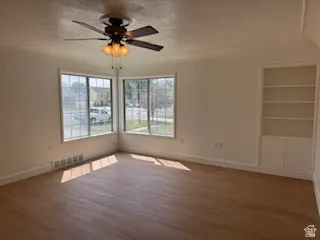 Unfurnished room with built in shelves, a textured ceiling, wood finished floors, and a ceiling fan