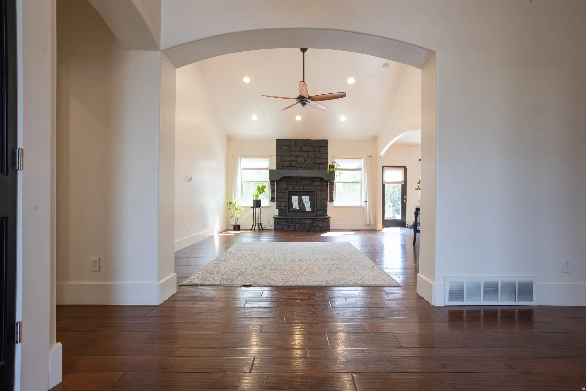 Unfurnished living room featuring a ceiling fan, lofted ceiling, recessed lighting, dark wood-type flooring, and a stone fireplace