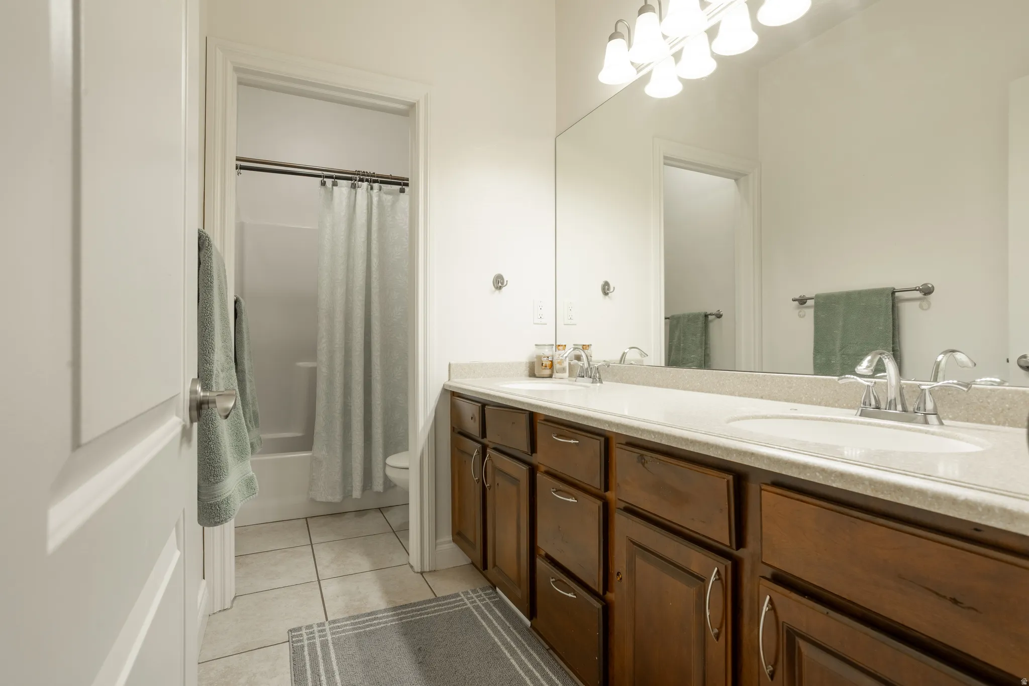Full bathroom featuring double vanity, light tile patterned floors, and shower / bath combination with curtain