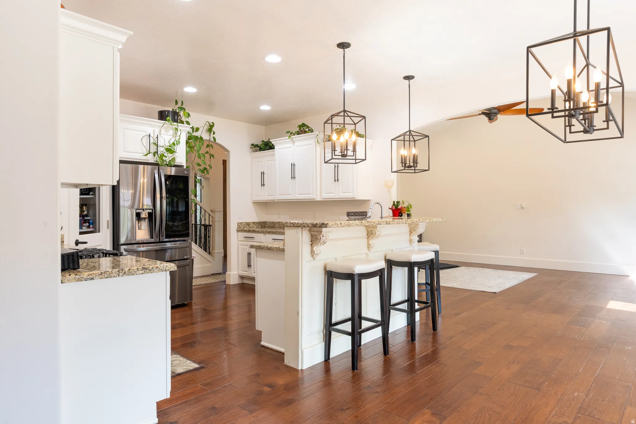 Kitchen with white cabinetry, stainless steel fridge with ice dispenser, light stone countertops, a breakfast bar, and hanging lights