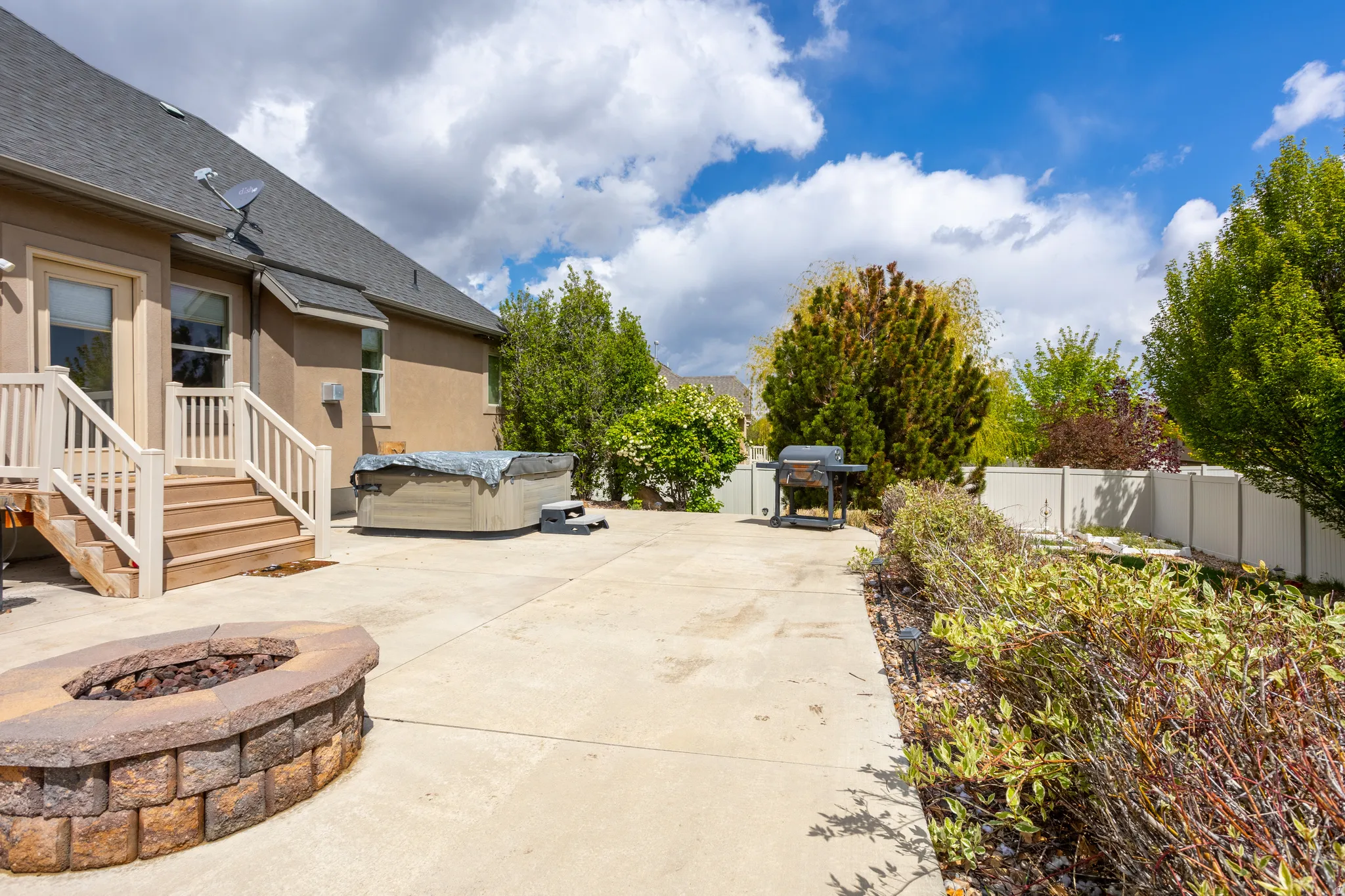 Fenced backyard featuring a hot tub, a fire pit, and grilling area
