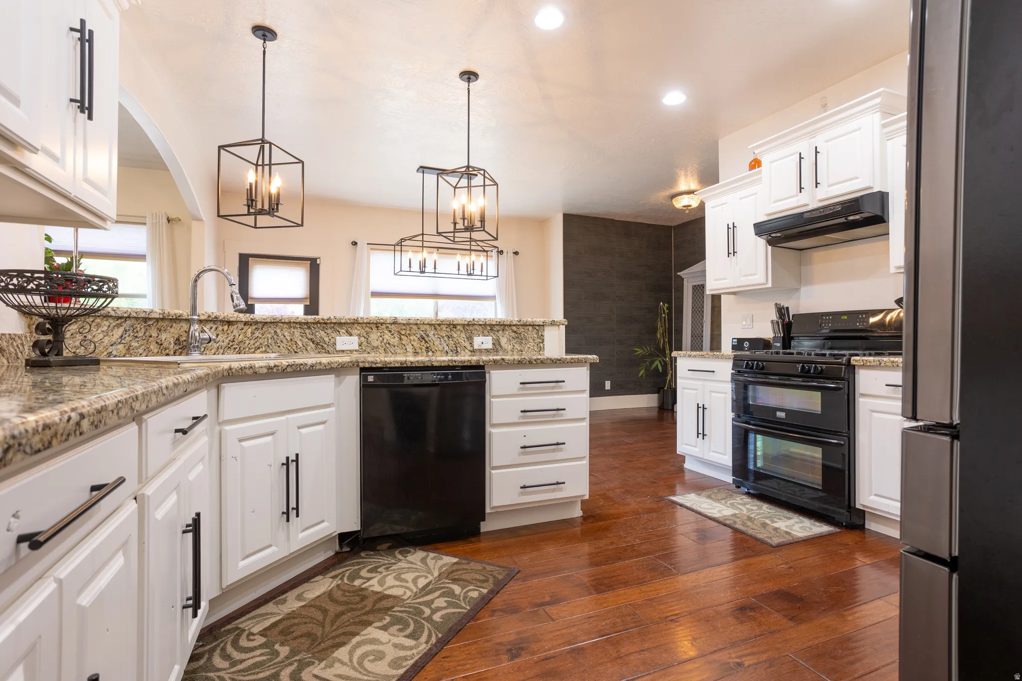 Kitchen featuring black appliances, white cabinetry, dark wood-style flooring, light stone countertops, and pendant lighting