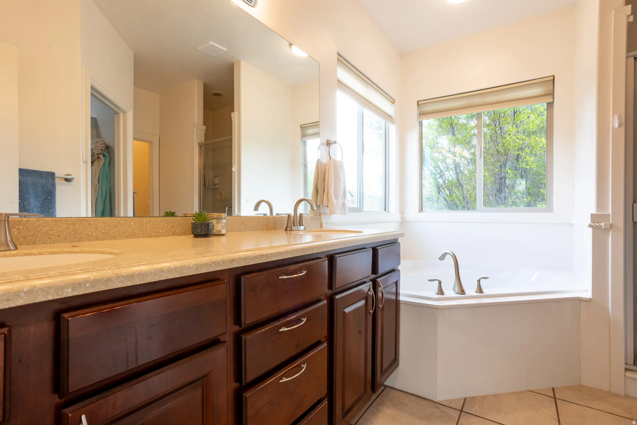 Bathroom featuring a stall shower, double vanity, a bath, and light tile patterned floors