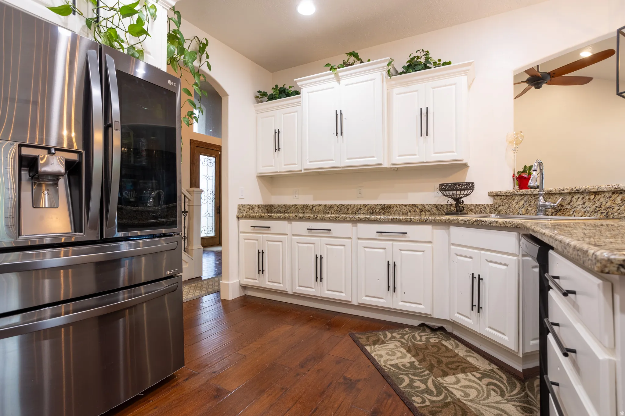Kitchen featuring stainless steel fridge, white cabinets, light stone countertops, dark wood-style flooring, and a ceiling fan