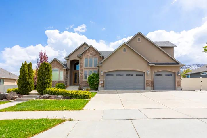 View of front of property featuring a garage, stucco siding, driveway, stone siding, and a gate