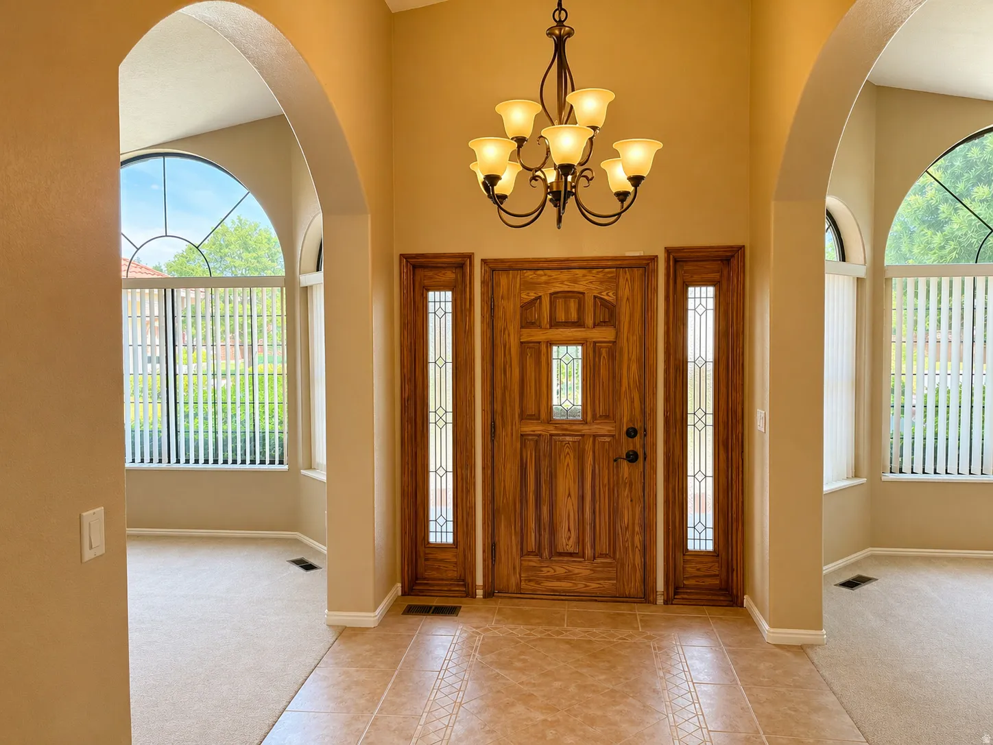 Foyer featuring light carpet, light tile patterned floors, a chandelier, and arched walkways