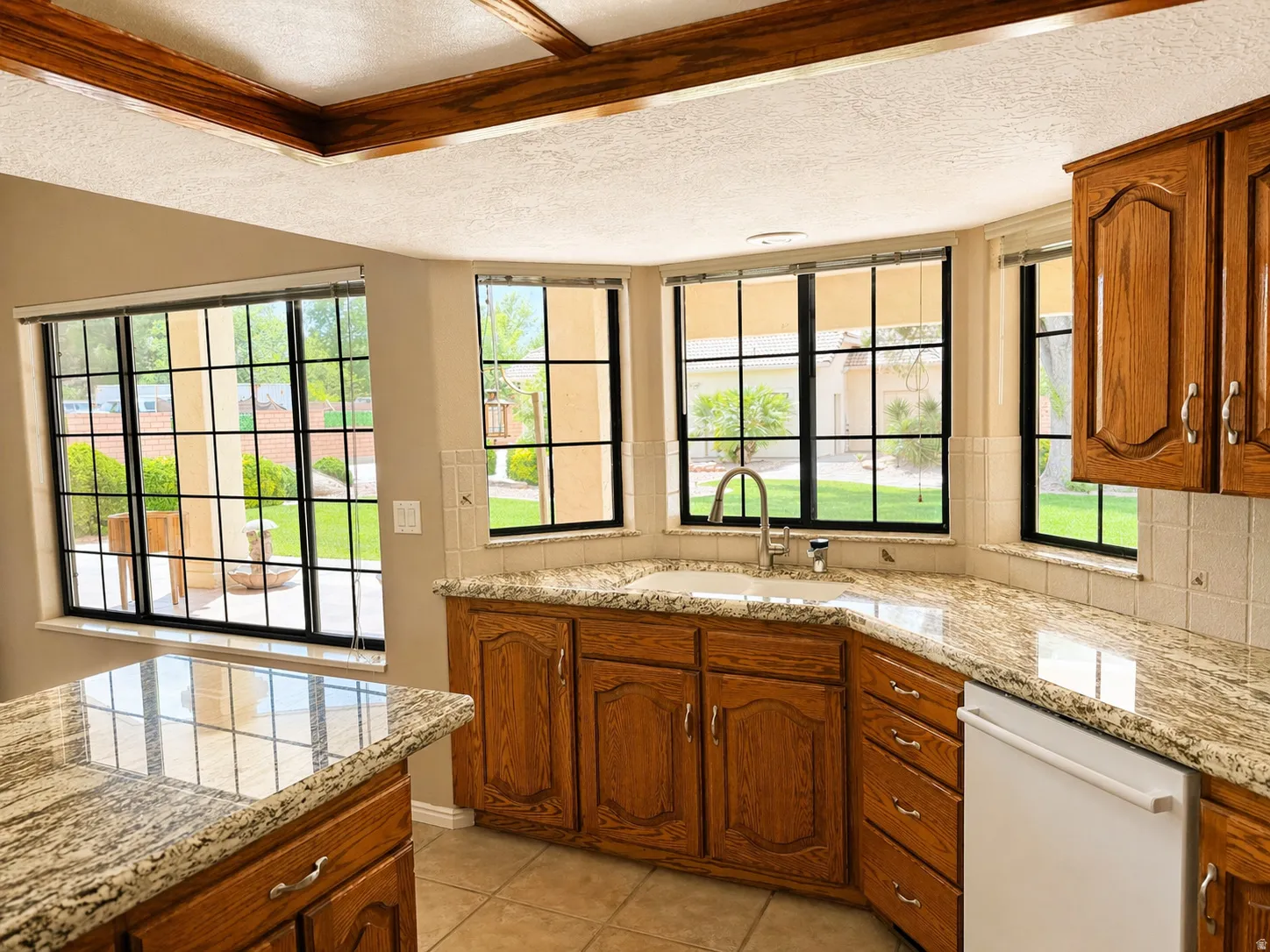 Kitchen with wood finish cabinetry, white dishwasher, tasteful backsplash, light stone counters, and a textured ceiling
