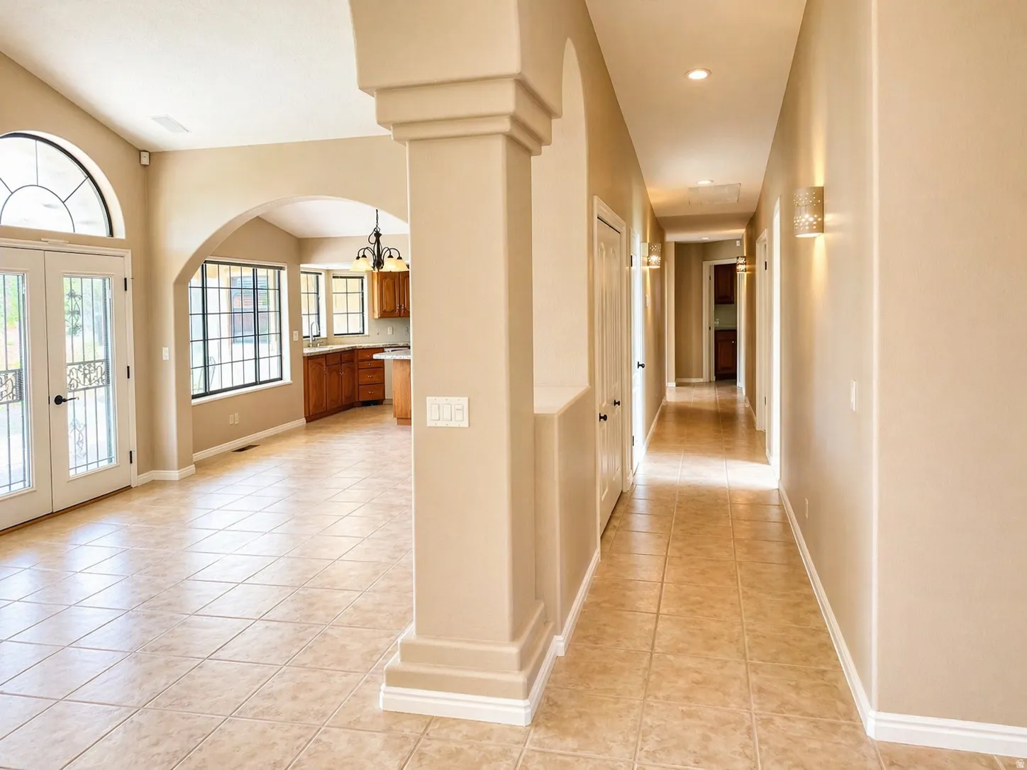 Hall featuring arched walkways, french doors, light tile patterned floors, and a chandelier