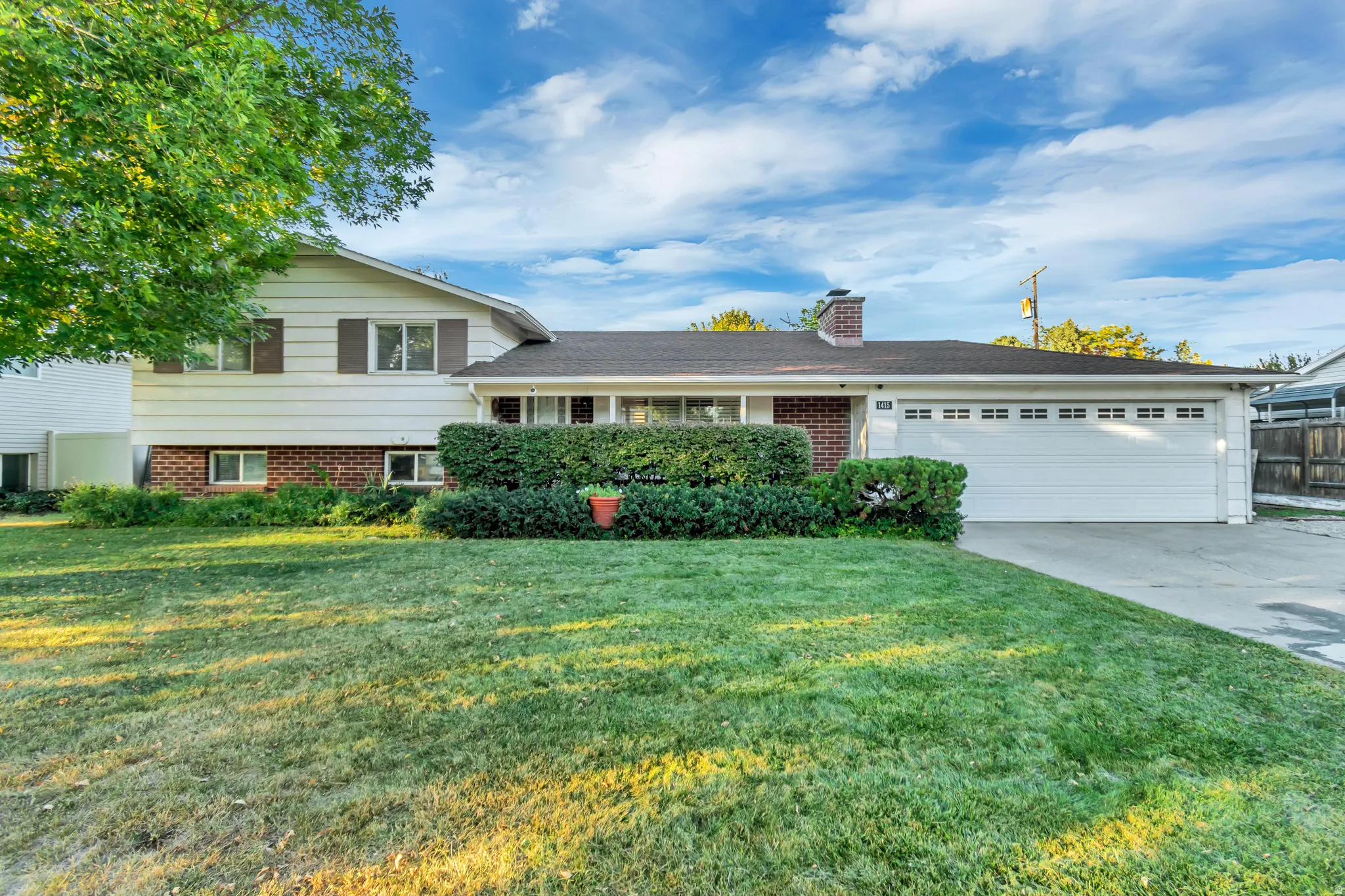 Split-level home with a front lawn, a chimney, concrete driveway, and brick siding