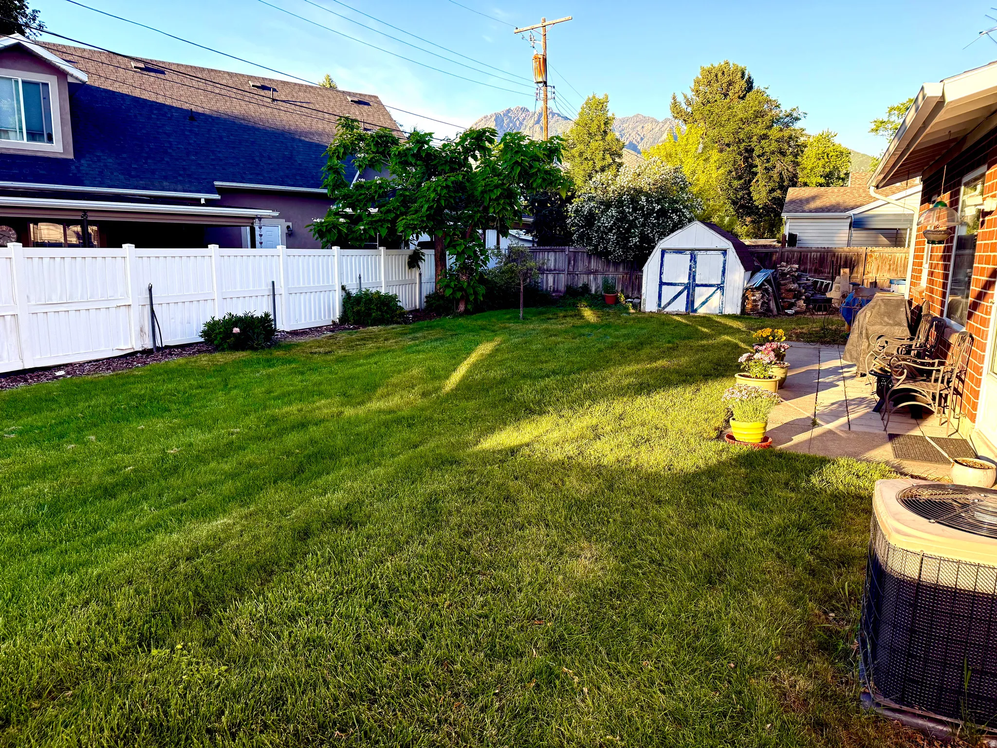 Expansive backyard featuring a large green lawn, a white vinyl privacy fence, and a patio area