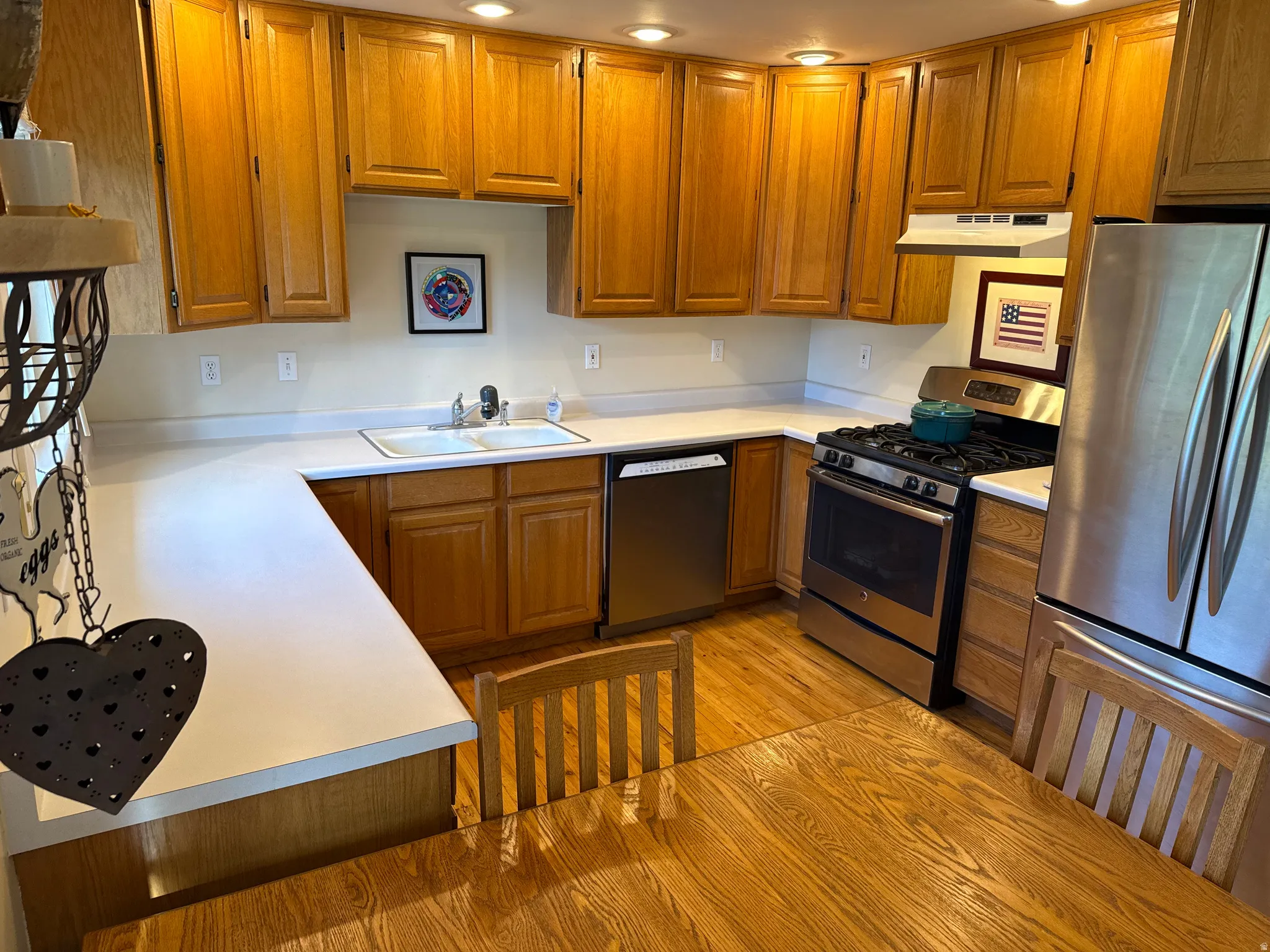 Open-concept kitchen featuring light wood cabinetry, white countertops, stainless steel appliances, and wood-finish flooring