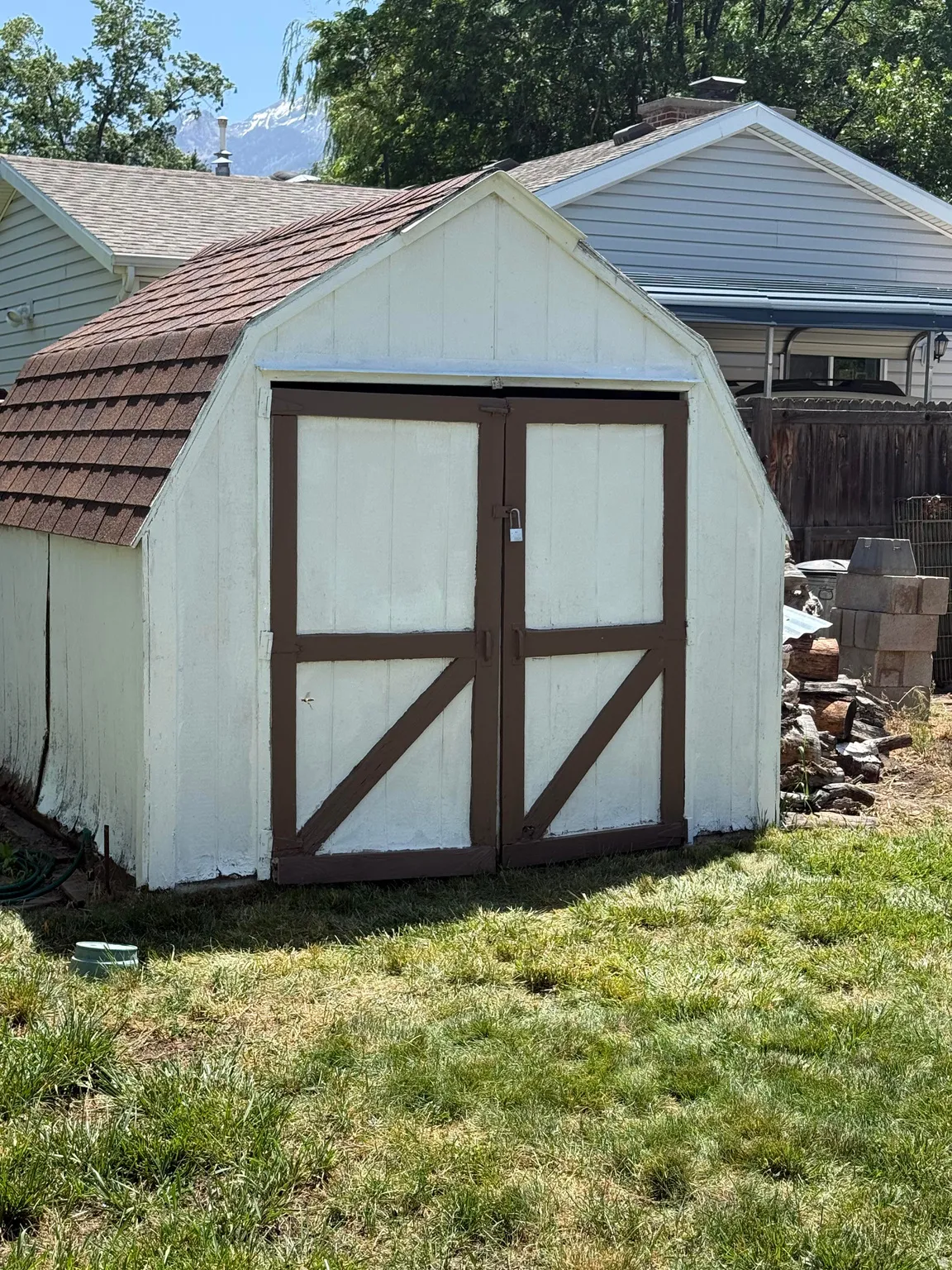 White storage shed with a gambrel roof and brown shingle finish