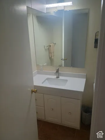 Vanity featuring a white cabinetry base, rectangular integrated sink, stone-finish countertop, single-handle brushed metal faucet, and wall-mounted vanity mirror with integrated lighting