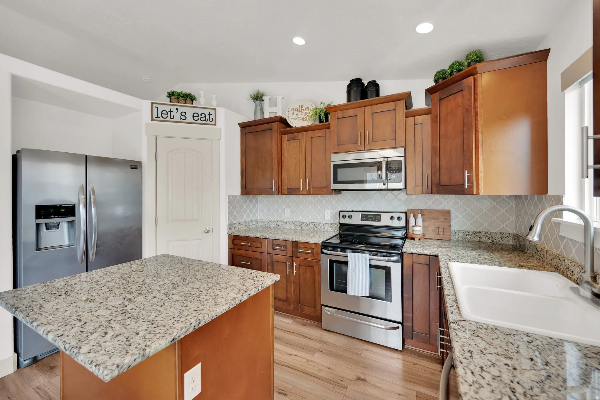 Kitchen with stainless steel appliances, light wood-style floors, light stone countertops, a kitchen island, and recessed lighting