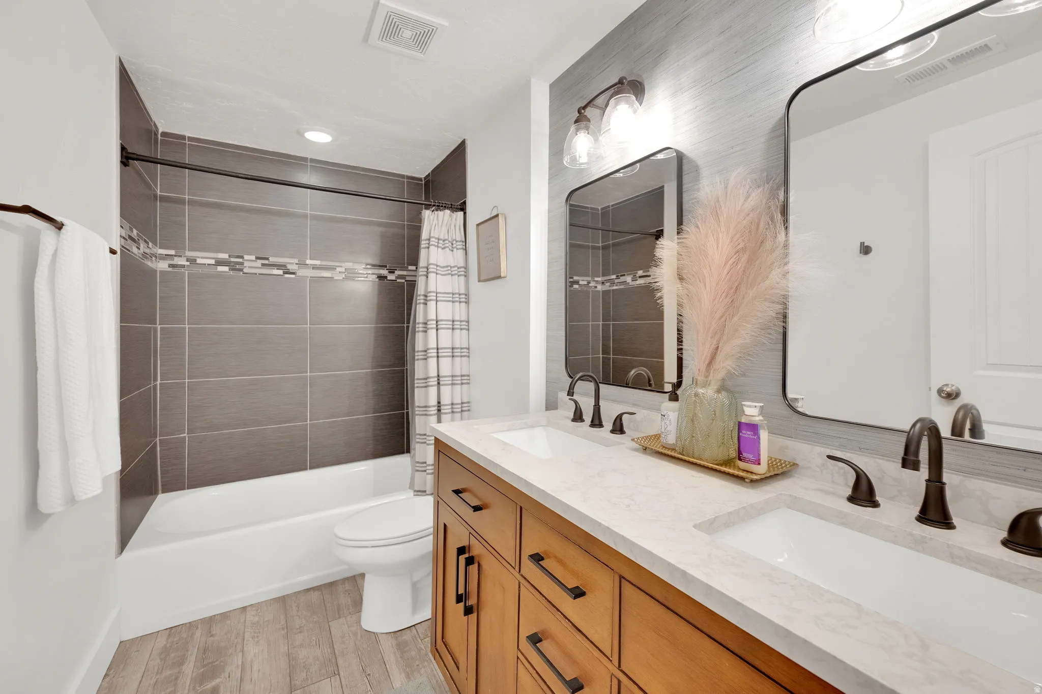 Full bathroom featuring double vanity, shower / bathtub combination with curtain, and light wood-style floors