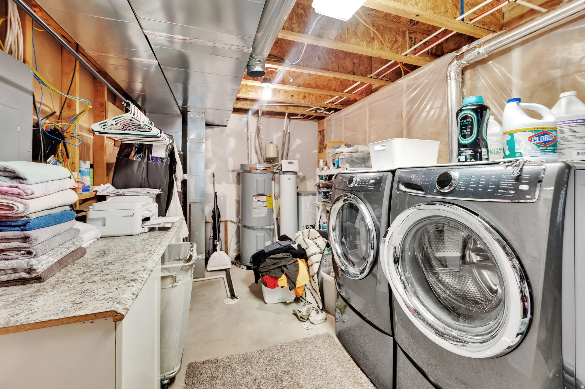 Laundry area with unfinished concrete floors, water heater, separate washer and dryer, and electric panel