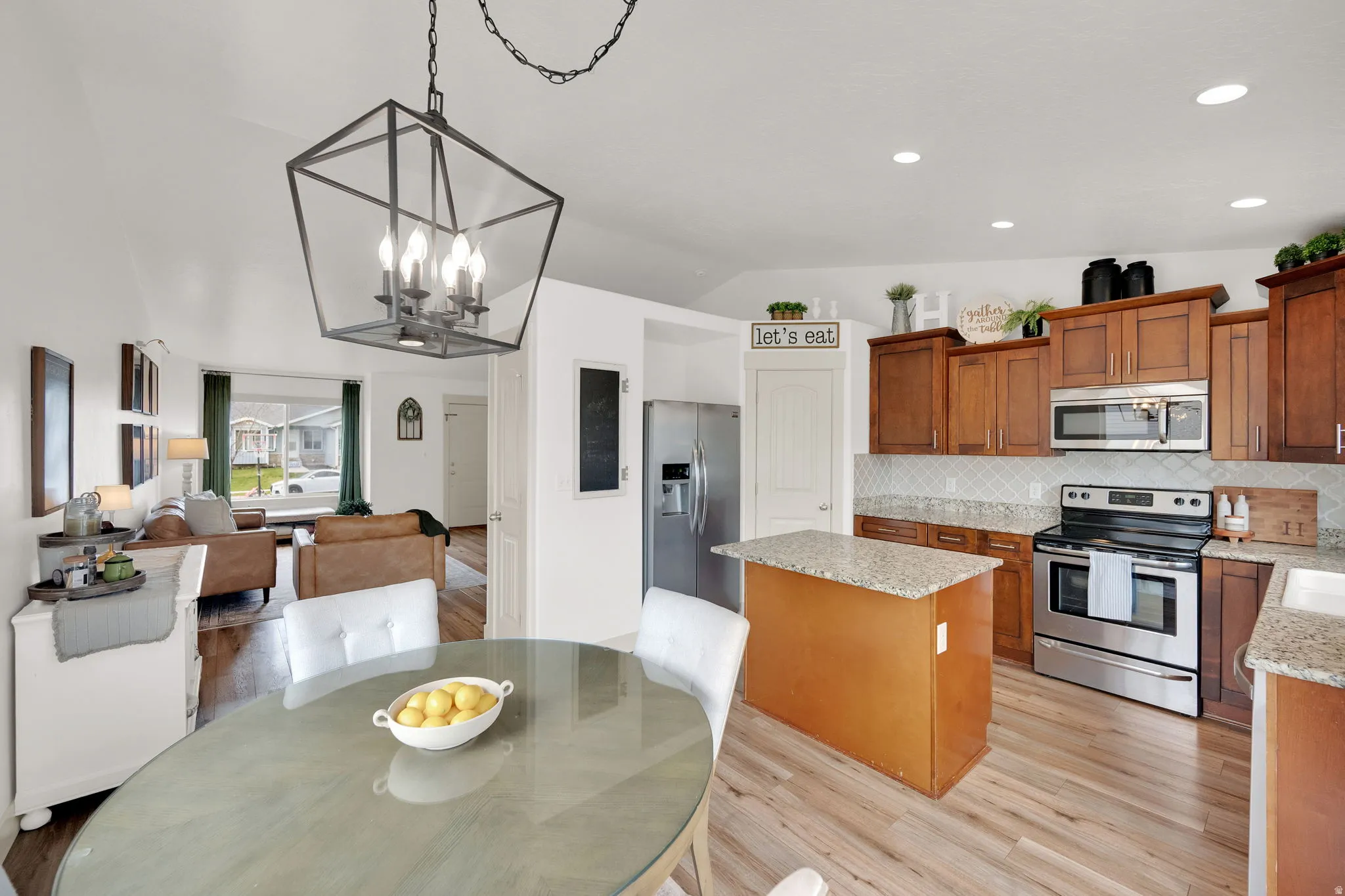 Kitchen with a center island, stainless steel appliances, lofted ceiling, wood finish cabinetry, and light stone counters