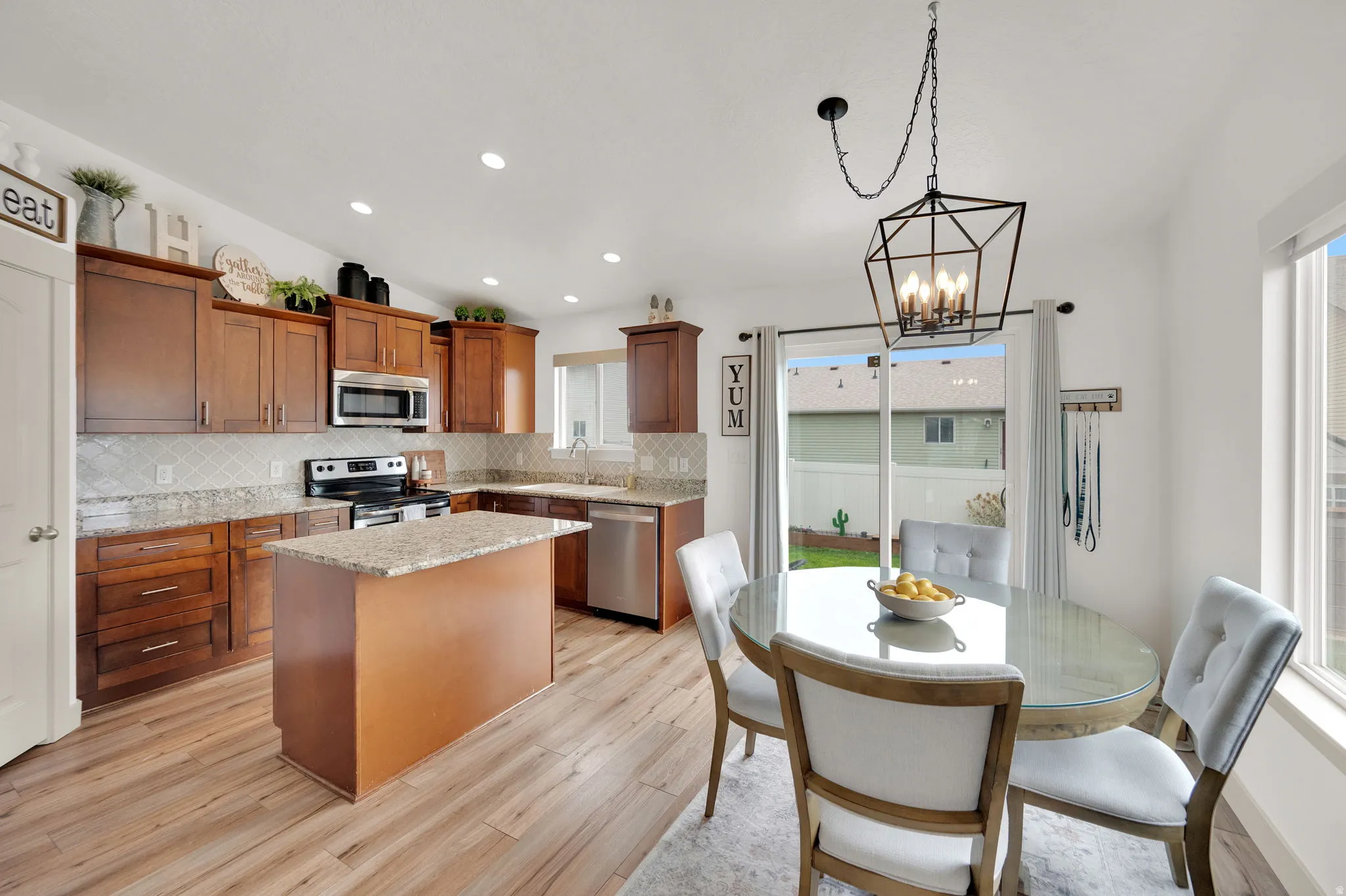 Kitchen featuring light stone countertops, stainless steel appliances, a kitchen island, wood finish cabinetry, and tasteful backsplash