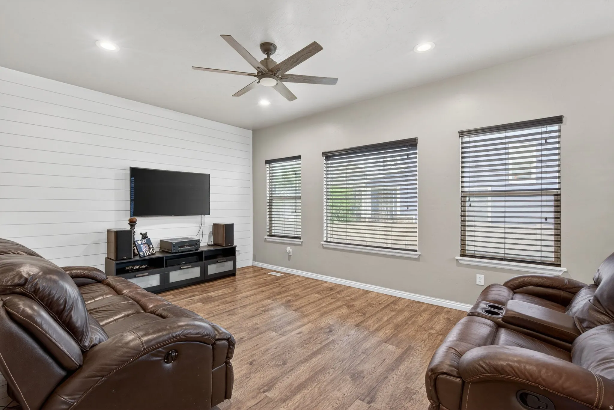 Living room with wooden walls, wood finished floors, recessed lighting, ceiling fan, and an accent wall