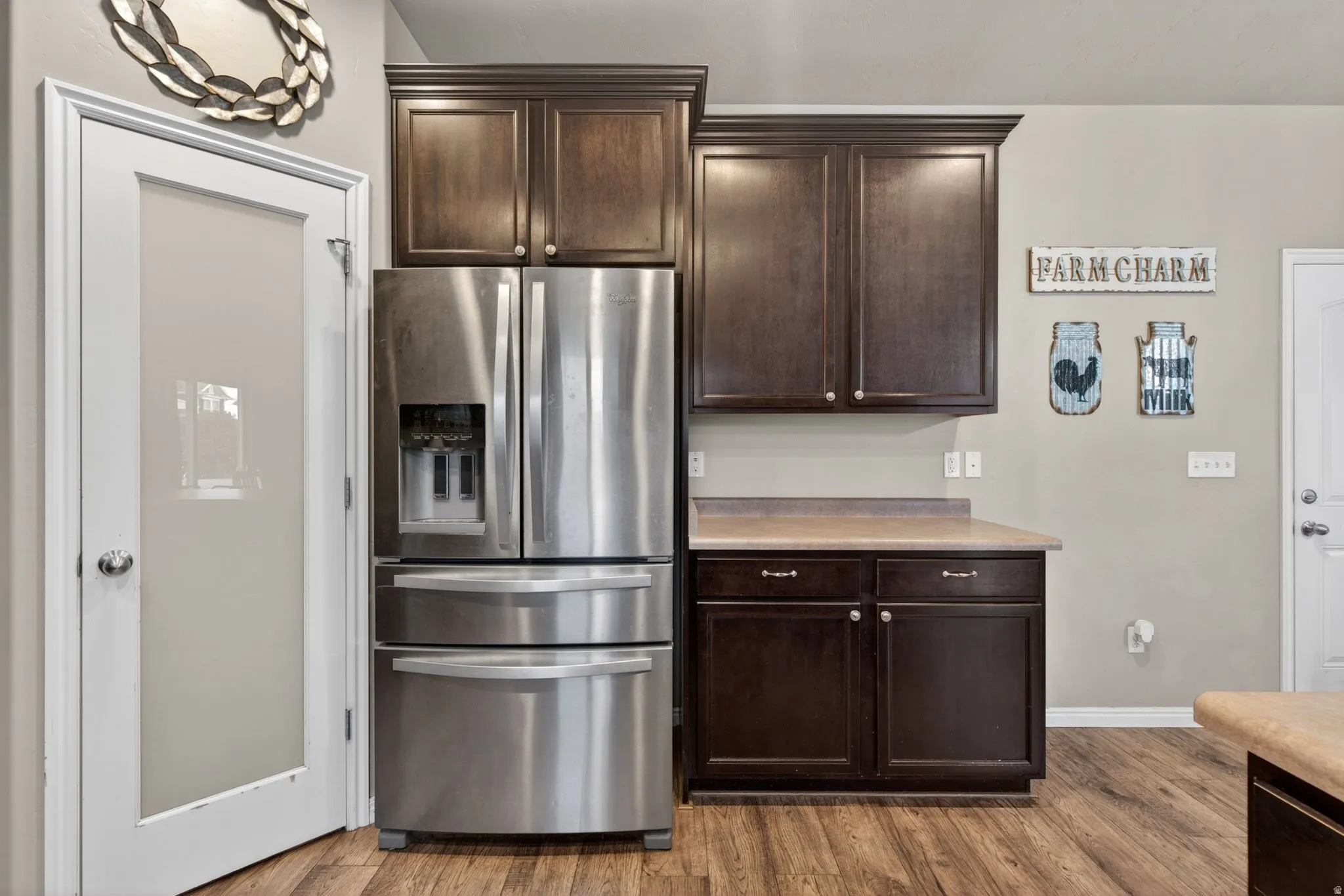 Kitchen featuring dark wood finish cabinetry, stainless steel fridge with ice dispenser, light countertops, and wood finished floors
