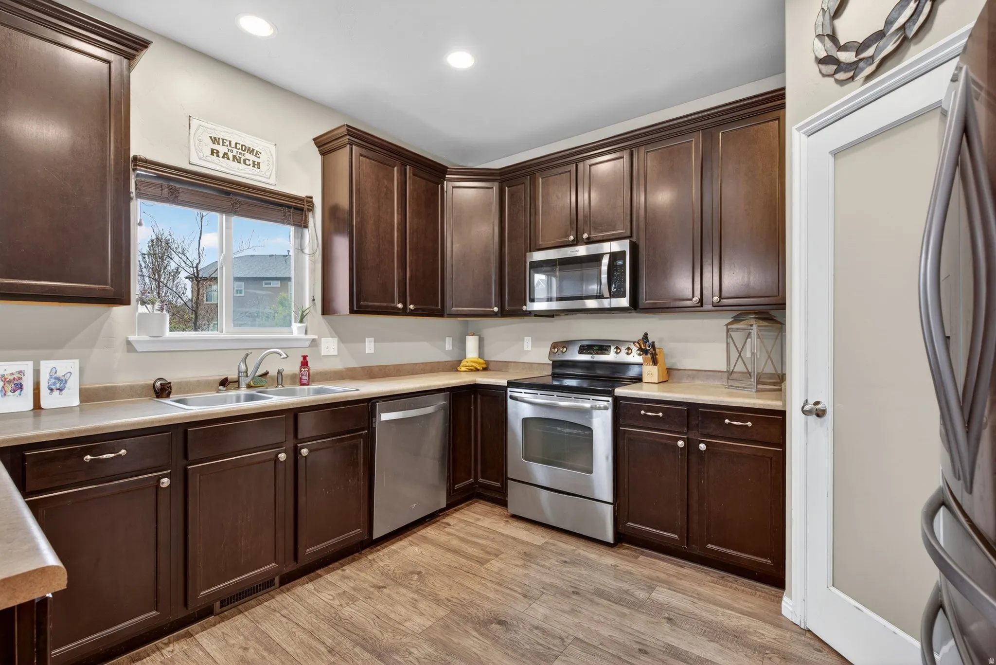 Kitchen with dark wood finish cabinetry, stainless steel appliances, light countertops, light wood finished floors, and recessed lighting