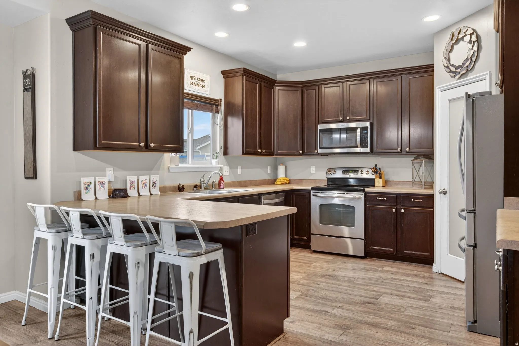 Kitchen with dark wood finish cabinets, a peninsula, a kitchen bar, stainless steel appliances, and light countertops