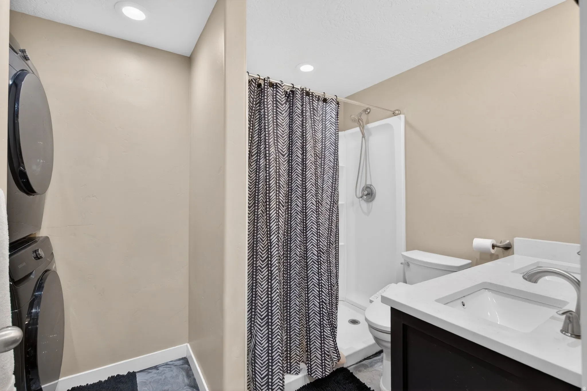 Full bath featuring double vanity, stacked washer / dryer, a shower stall, and recessed lighting