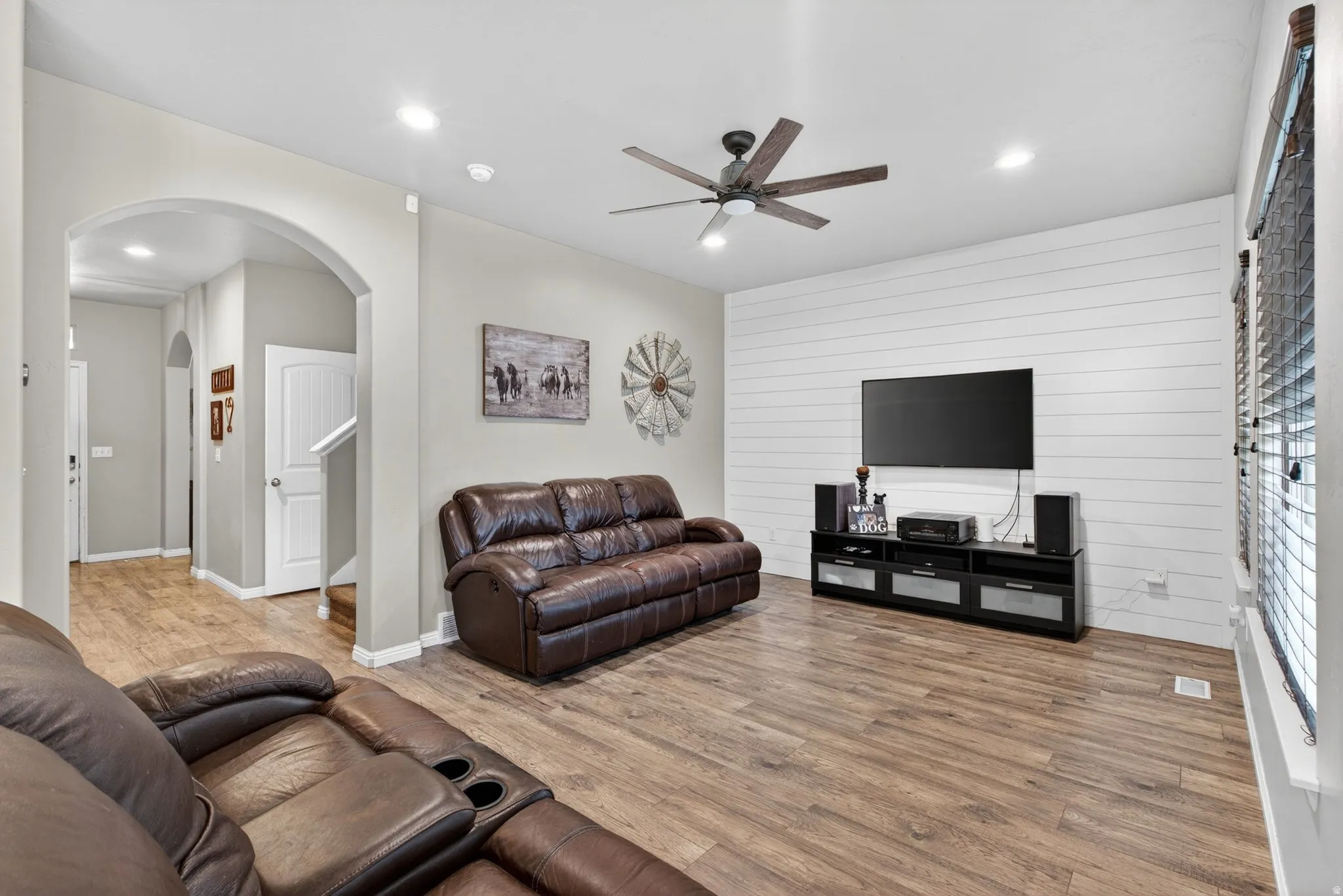 Living room with ceiling fan, light wood-style floors, recessed lighting, wooden walls, and arched walkways