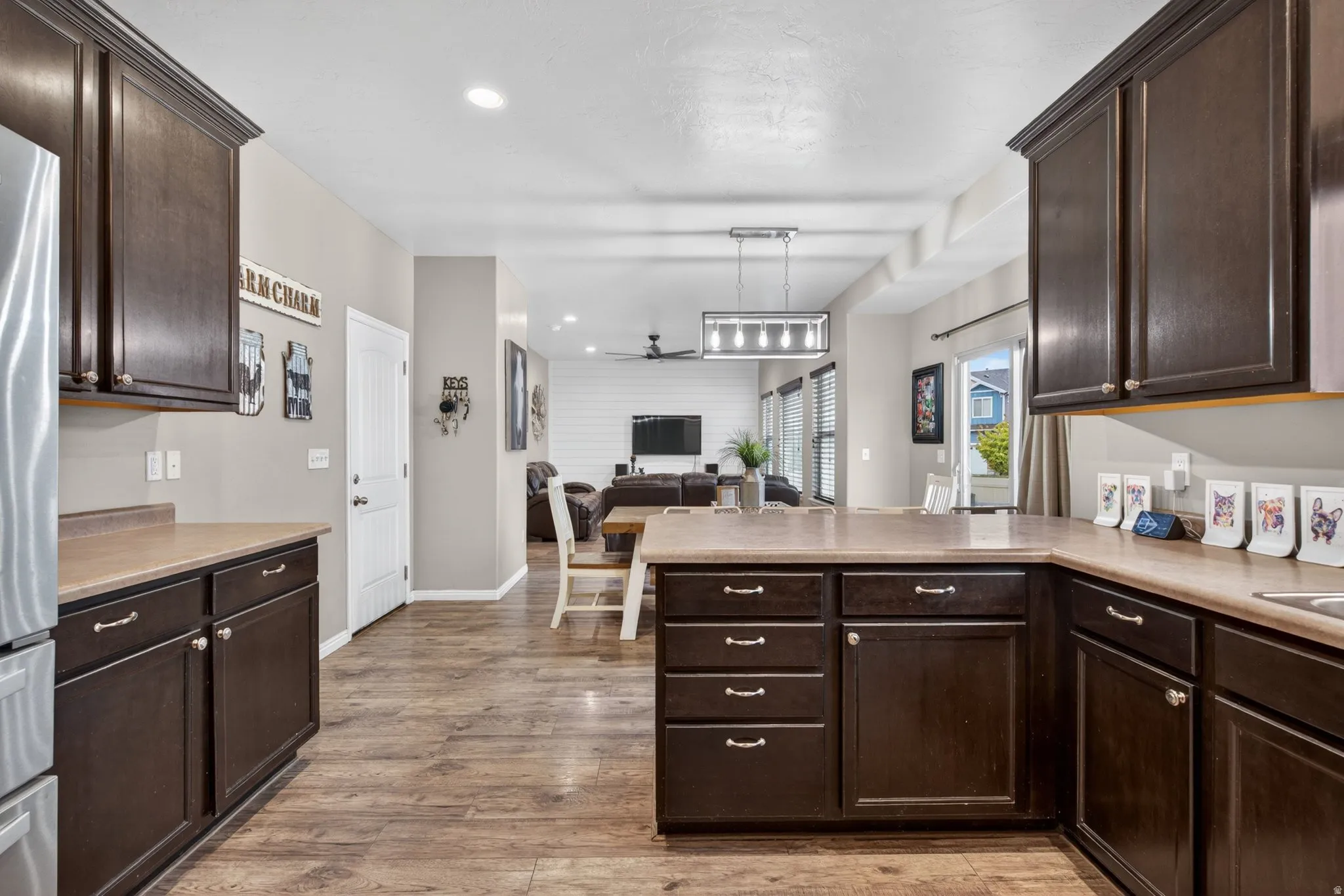 Kitchen featuring dark wood finish cabinets, a peninsula, open floor plan, light countertops, and a ceiling fan