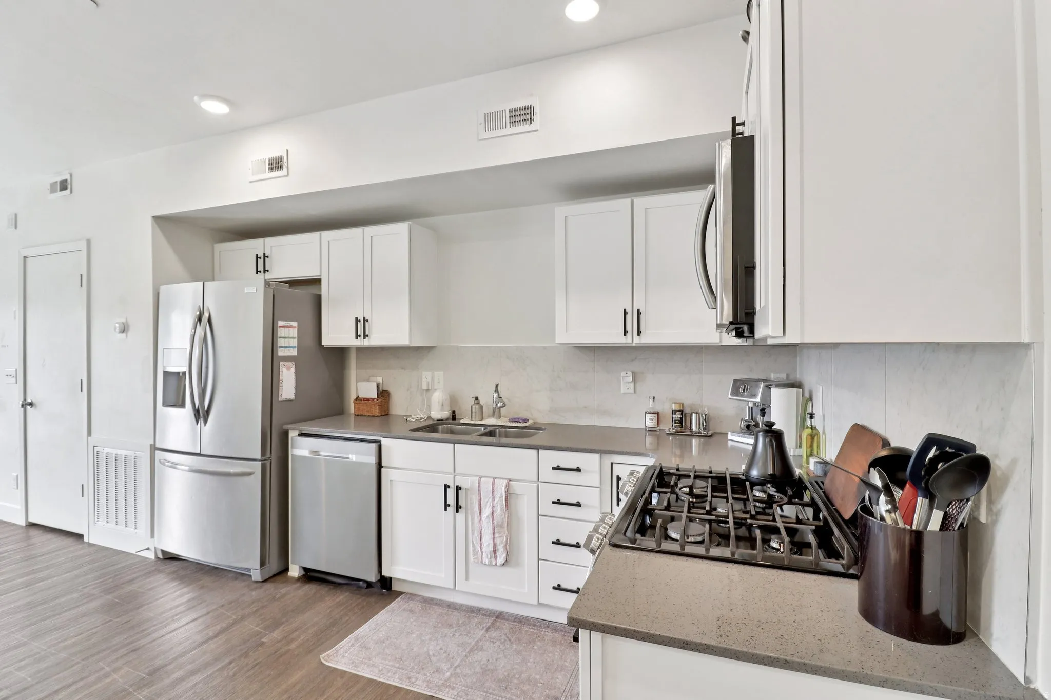 Kitchen with white cabinets, light stone counters, stainless steel appliances, light wood-style floors, and tasteful backsplash
