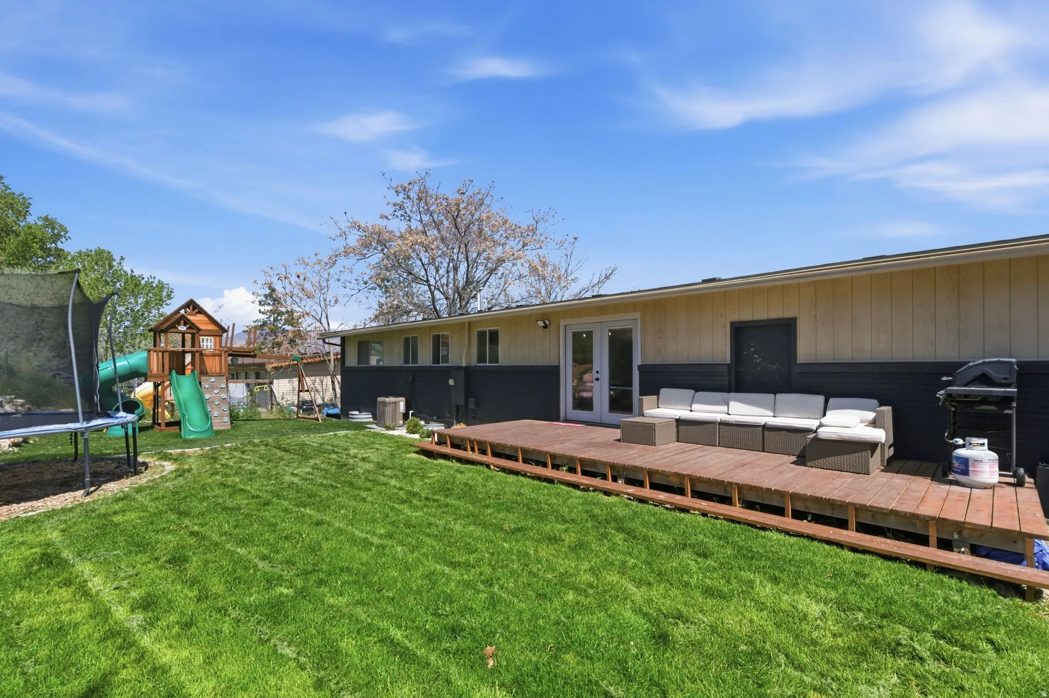 Back of house with a trampoline, outdoor seating, french doors, a wooden deck, and a yard