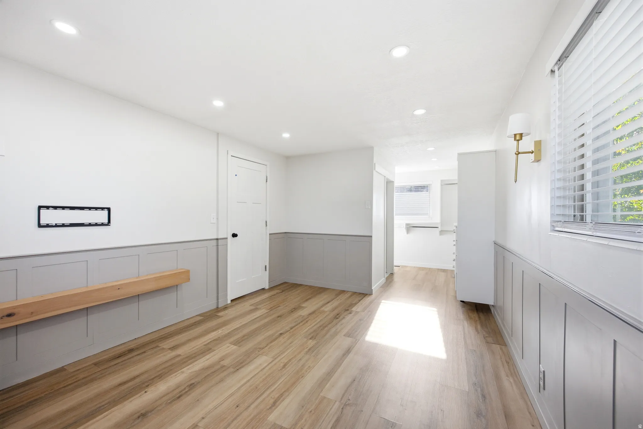 Spacious room with wood-finish flooring, recessed lighting, and white walls featuring gray wainscoting