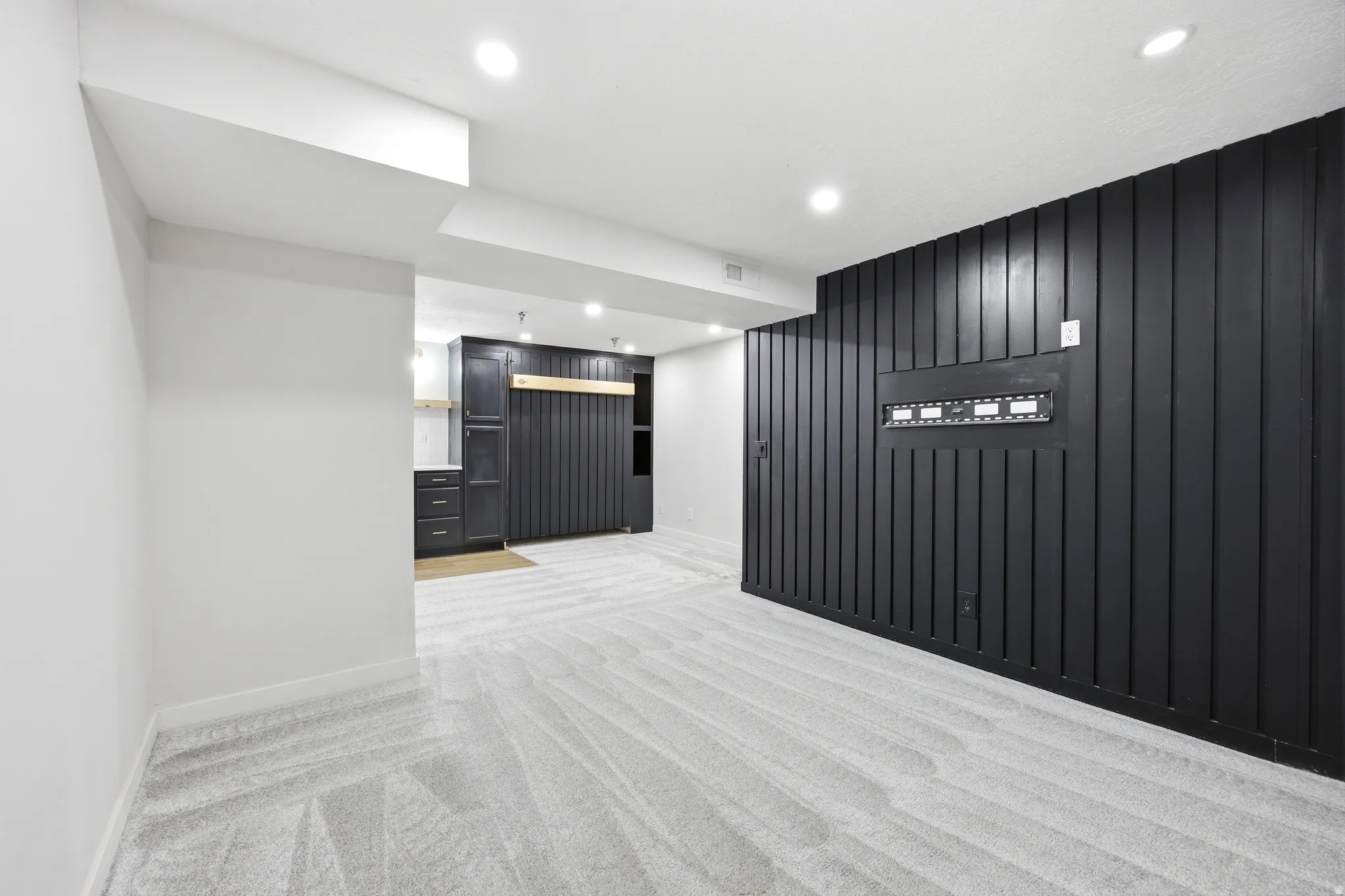 Contemporary living area featuring patterned carpet, recessed lighting, and a striking black accent wall with vertical paneling