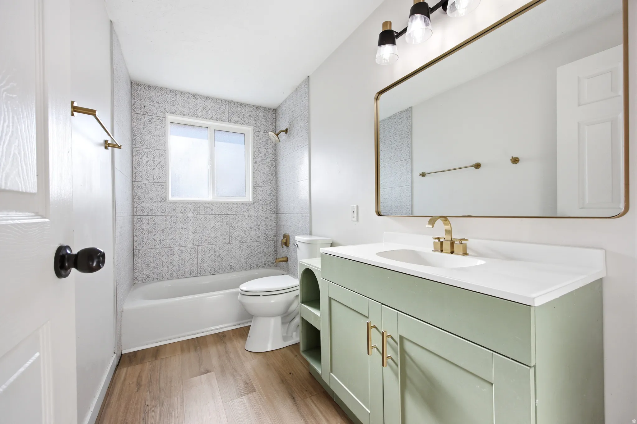 Light-filled bathroom featuring a single vanity with a pale green cabinet, a white countertop, and gold-finish hardware