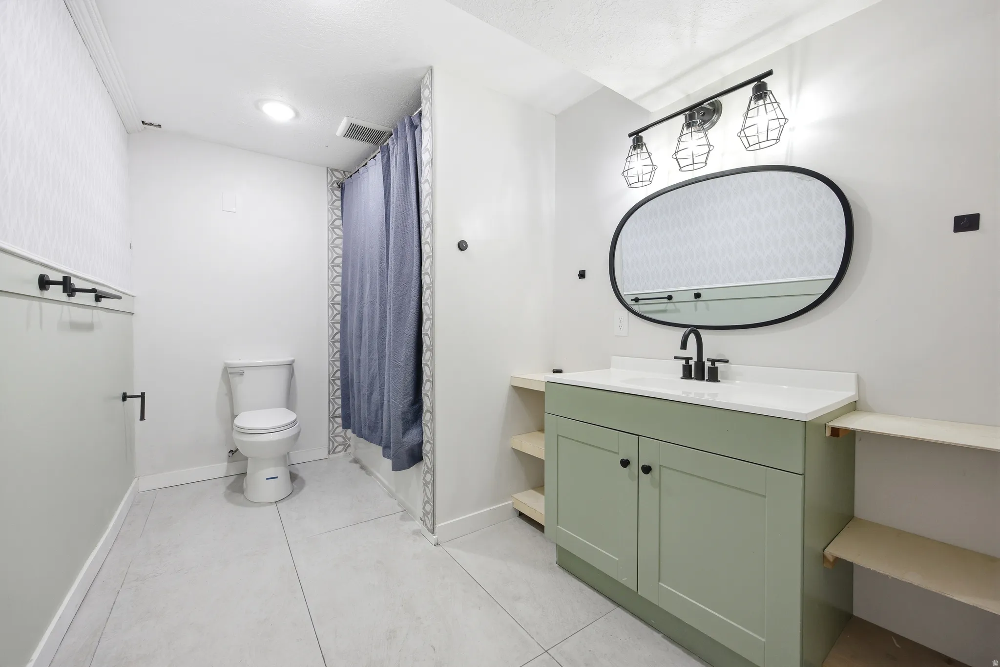 Bathroom featuring a sage green vanity with a white countertop and a black-framed oval mirror