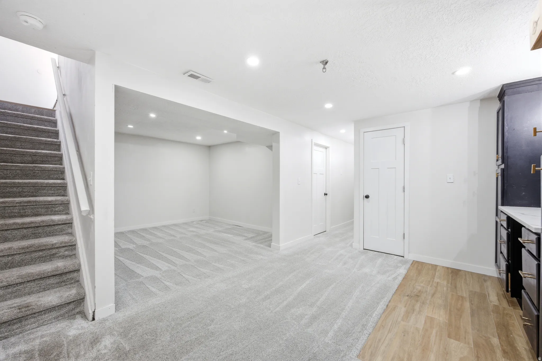 Versatile lower level featuring recessed lighting, plush carpet flooring, a dedicated stairwell, multiple white panel doors, and a built-in cabinetry unit with a light-toned countertop