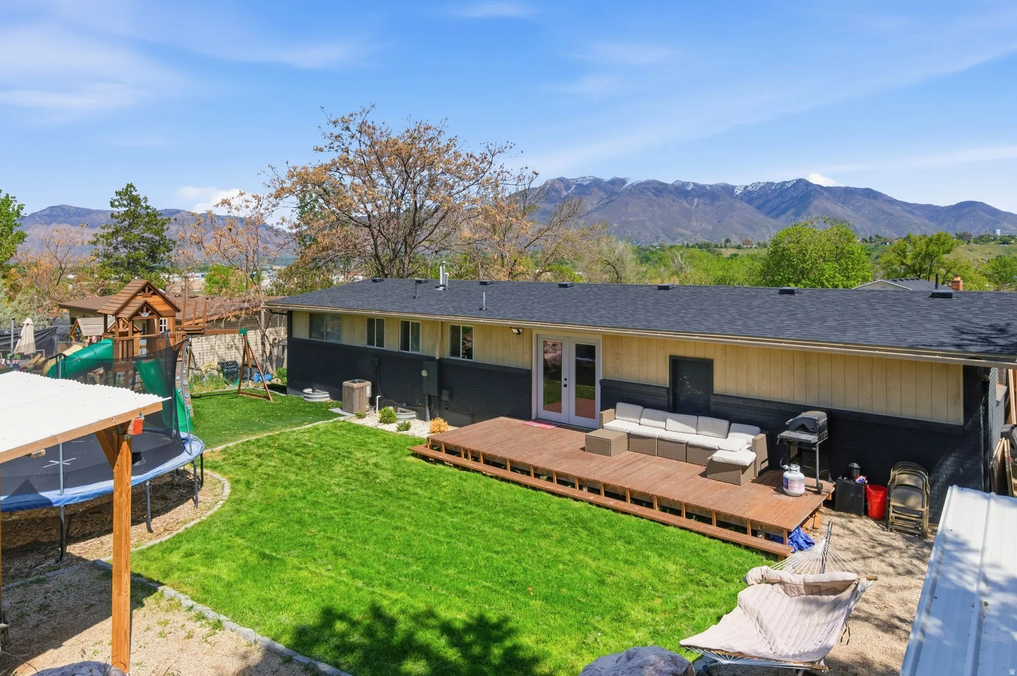 Back of property featuring a trampoline, an outdoor hangout area, a playground, a deck with mountain view, and french doors