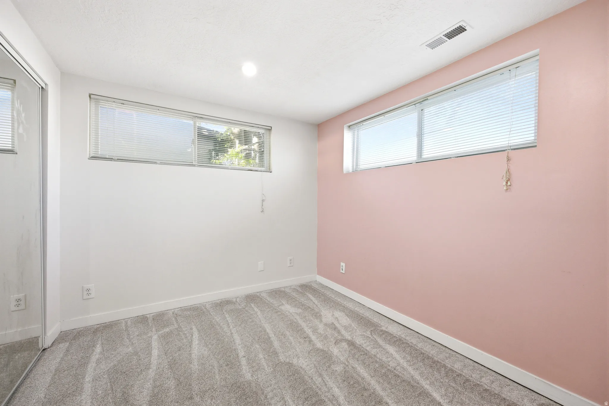 Carpeted interior space featuring a mirrored closet, two windows with blinds, a white ceiling with recessed lighting, and a neutral color palette