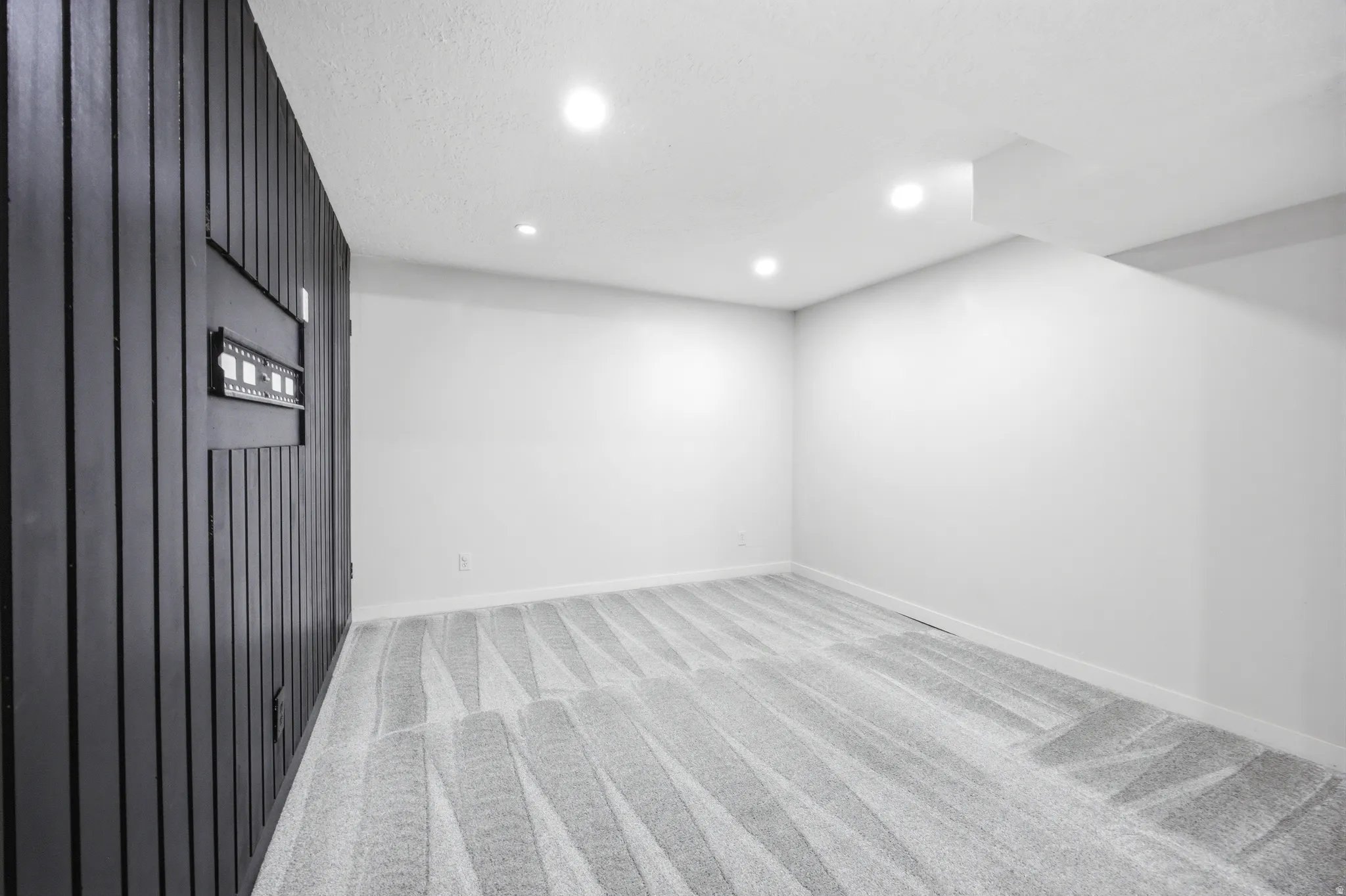 Recessed lighting illuminates a spacious room featuring a distinctive black paneled accent wall